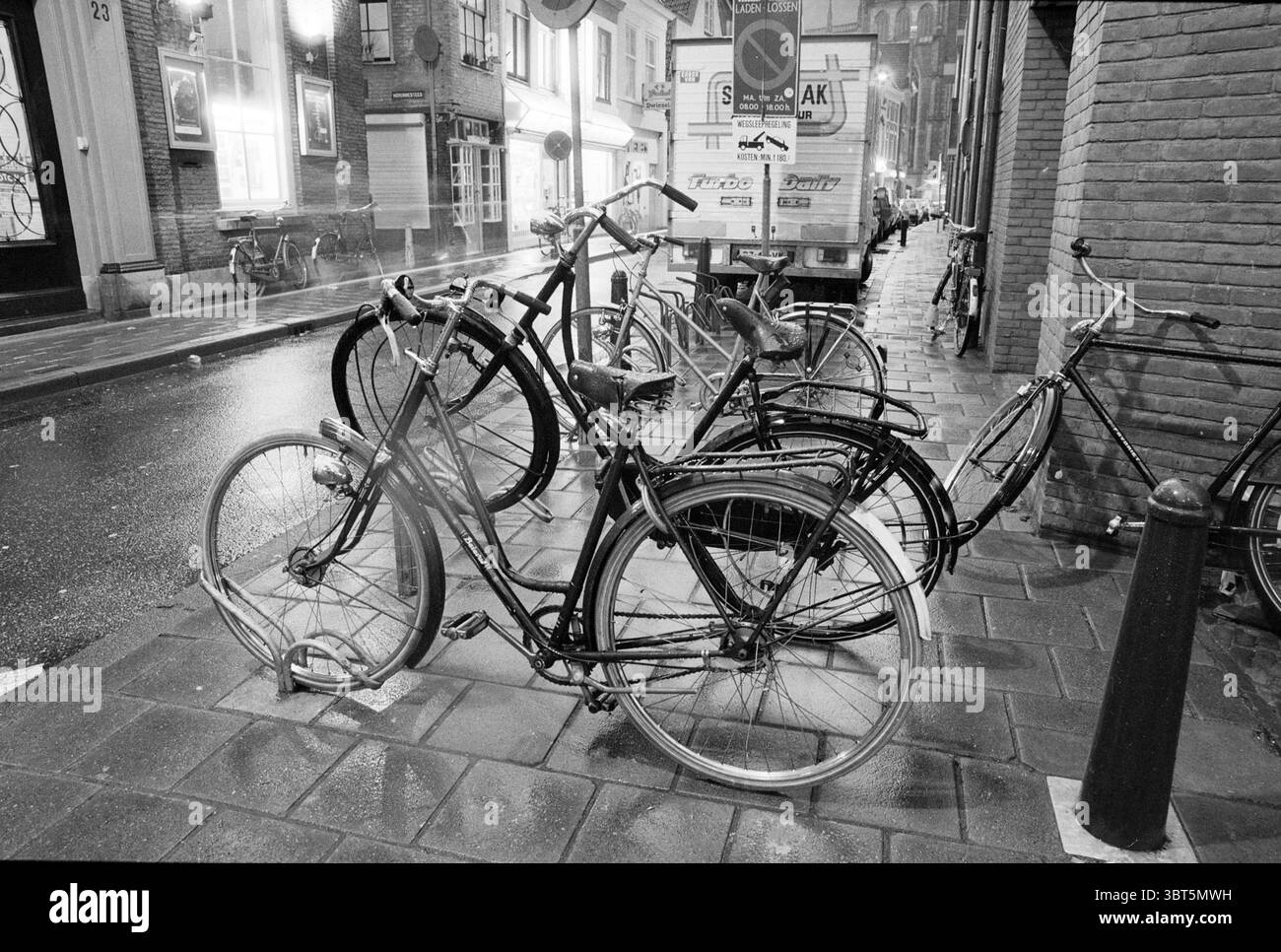 Stand per biciclette posizionato in modo errato in Smedestraat Cycling Paths Cyclists Haarlem Smedestraat Paesi Bassi, Whizgle News, Dutch Desk, Paesi Bassi, 1950 - 2000 il 06-04-1989. Questi argomenti sono mostrati nell'immagine. La scena raffigura una strada stretta e urbana, caratterizzata dalla sua pavimentazione acciottolata che risplende dalle recenti precipitazioni. Un gruppo di biciclette è appoggiato su una robusta ringhiera in metallo, i loro telai variavano nel design, suggerendo stili e usi diversi. Alcune biciclette sono dotate di manubri verticali tradizionali, mentre altre sono dotate di manubri da corsa, che fanno pensare alla comunità diversificata che fa la differenza Foto Stock