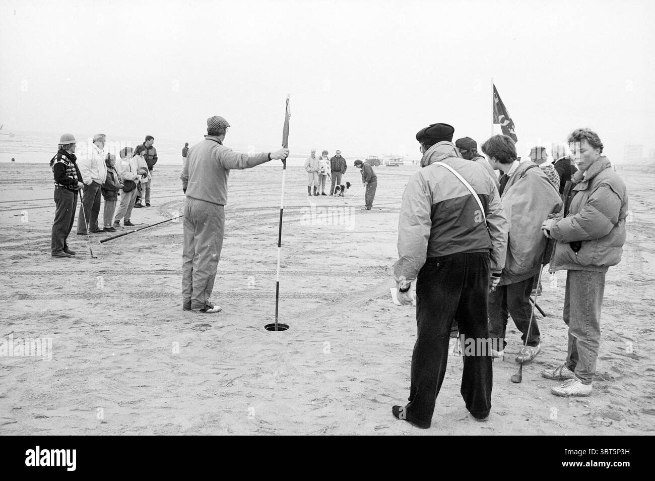Gare di golf spiaggia Zandvoort Golf Golf Zandvoort, Whizgle News, Dutch Desk, Paesi Bassi, 1950 - 2000 il 19-02-1988. L'immagine contiene questi argomenti. La scena raffigura un gruppo di individui riuniti su una spiaggia sabbiosa, avvolti in un'atmosfera nebbiosa che conferisce una qualità silenziosa e attenuata all'ambiente. La superficie sabbiosa, di colore pallido, contrasta con l'abbigliamento scuro e chiaro indossato dalle persone, che sfoggiano una gamma di stili, dallo sportivo al casual. Diverse cifre sono impegnate in quella che sembra essere una qualche forma di attività organizzata, che probabilmente coinvolge una competizione o un gioco, come indi Foto Stock