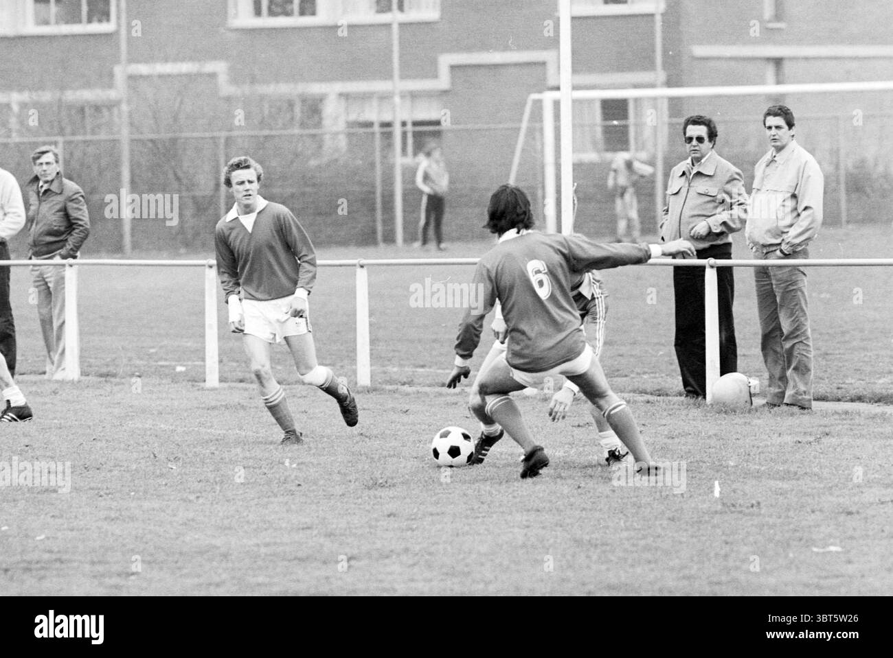 IJmuiden - GVVV Football IJmuiden, Whizgle News, Dutch Desk, Paesi Bassi, 1950 - 2000 il 13-05-1979. L'immagine include questi argomenti. La scena cattura un momento vivace su un campo da calcio erboso, dove due giocatori sono attivamente impegnati nel gioco. Un giocatore, vestito con una maglia rossa adornata con il numero 6, sta manovrando abilmente la palla da calcio, il cui obiettivo è evidente mentre si prepara a passare o dribblare. Il giocatore avversario, che indossa una maglia blu, è pronto ad intercettare, dimostrando un'espressione intenzionale che trasmette spirito competitivo. Sullo sfondo, diversi spettatori guardano con attenzione, t Foto Stock