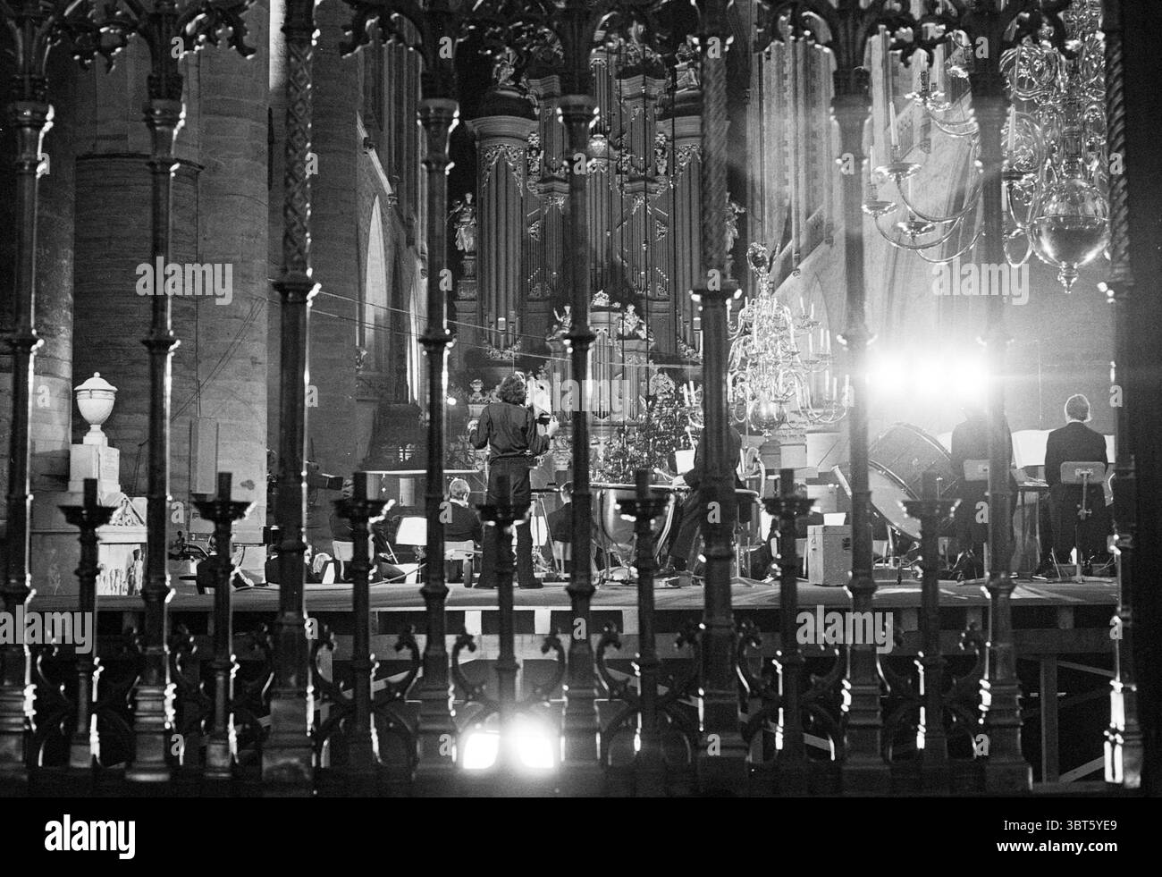 Concerto classico nella chiesa di Grote (Bavo) con registrazione televisiva., Whizgle News, Dutch Desk, Paesi Bassi, 1950 - 2000. Questi argomenti sono mostrati nell'immagine. La scena è ambientata all'interno di un grande spazio ornato, probabilmente una cattedrale o una grande sala, caratterizzata da alti soffitti e intricati elementi architettonici. Gli interni sono illuminati da una combinazione di luce soffusa e ambientale e spot più mirati che evidenziano varie caratteristiche. In primo piano, un'elaborata ringhiera in ferro battuto crea una divisione tra lo spettatore e l'area oltre, aggiungendo un senso di profondità e inquadrando la scena. L'intrica Foto Stock Concerto classico nella chiesa di Grote (Bavo) con registrazione televisiva., Whizgle News, Dutch Desk, Paesi Bassi, 1950 - 2000. Questi argomenti sono mostrati nell'immagine. La scena è ambientata all'interno di un grande spazio ornato, probabilmente una cattedrale o una grande sala, caratterizzata da alti soffitti e intricati elementi architettonici. Gli interni sono illuminati da una combinazione di luce soffusa e ambientale e spot più mirati che evidenziano varie caratteristiche. In primo piano, un'elaborata ringhiera in ferro battuto crea una divisione tra lo spettatore e l'area oltre, aggiungendo un senso di profondità e inquadrando la scena. L'intrica Foto Stock