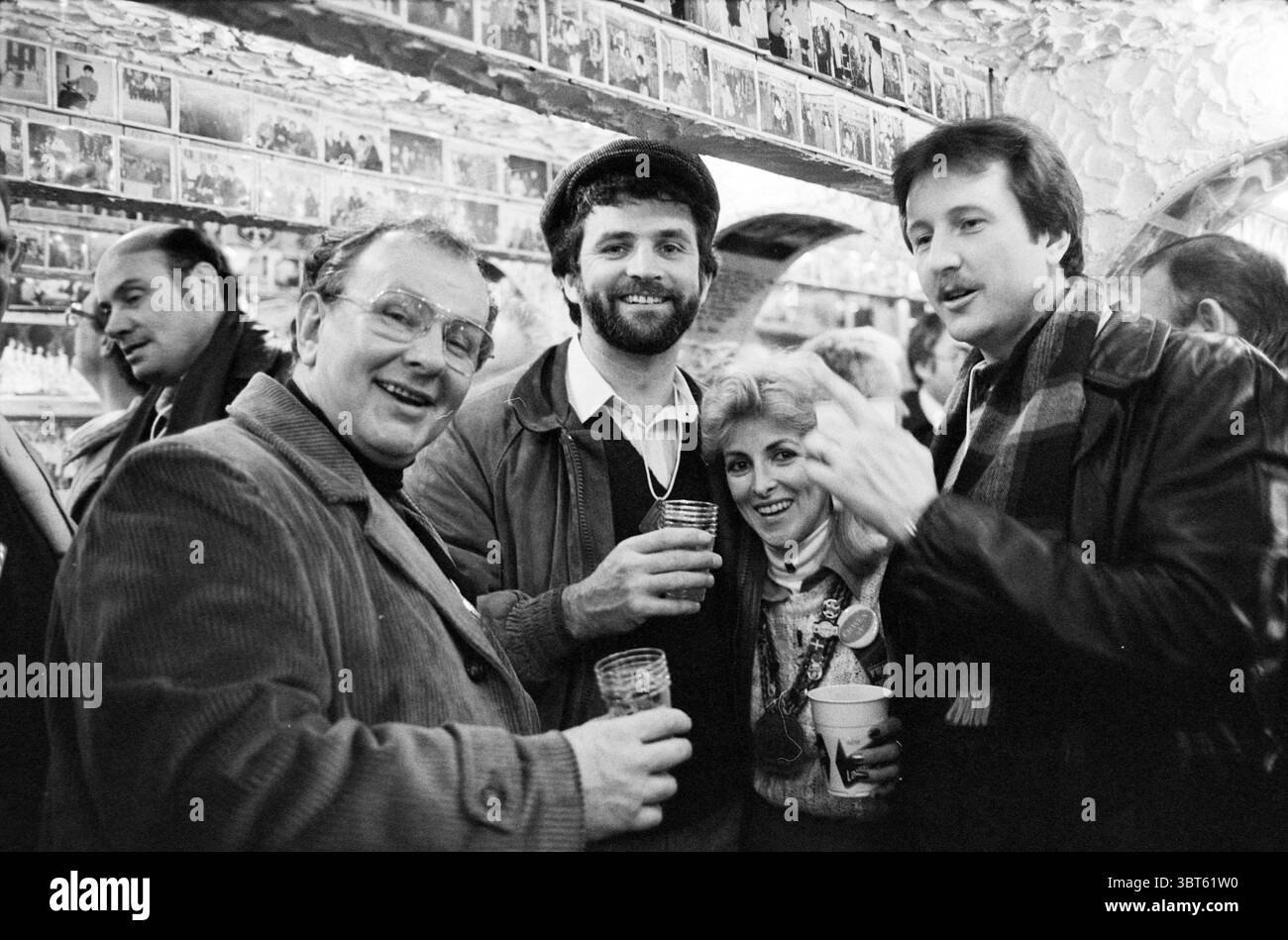 Winter Carnival Quebec Canada Carnival Quebec Canada, Whizgle News, Dutch Desk, Paesi Bassi, 1950 - 2000 il 02-1982. Questi sono gli elementi dell'immagine. La scena presenta un vivace ritrovo in un bar accogliente e animato. Un gruppo di quattro individui si trova in primo piano, ognuno con un drink, e le sue espressioni irradiano gioia e cameratismo. L'ambiente è caratterizzato da un'illuminazione calda e intima creata da soffici sistemi di illuminazione sopraelevati, che creano ombre delicate che esaltano l'atmosfera invitante. Le pareti sono adornate da numerose fotografie in bianco e nero, aggiungendo un touc nostalgico Foto Stock
