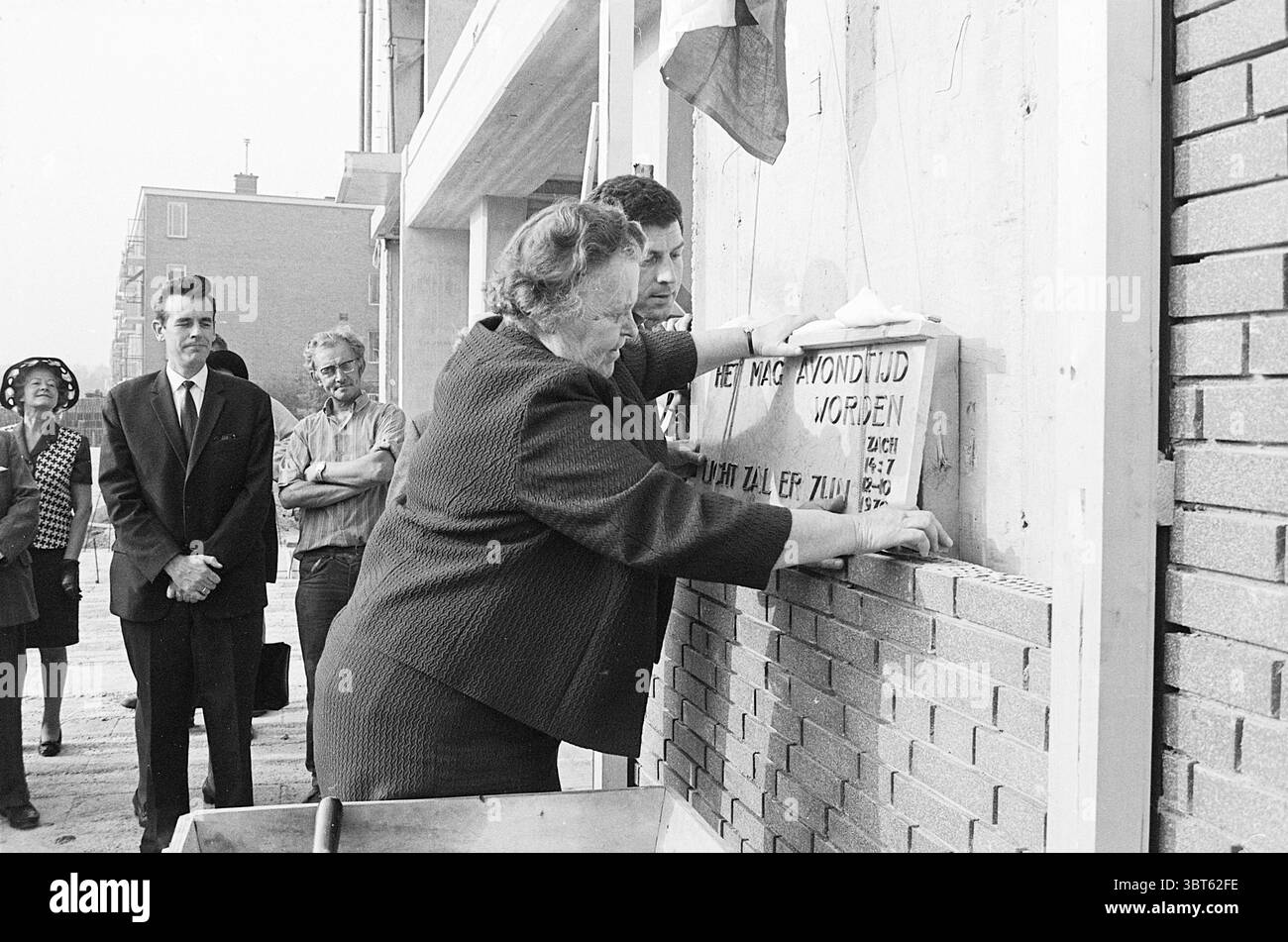 1st Stone Schoterhof First Stone, Whizgle News, Dutch Desk, Paesi Bassi, 1950 - 2000 il 12-10-1970. Questi argomenti sono mostrati nell'immagine. La scena cattura un momento significativo durante un evento cerimoniale incentrato sulla posa di una pietra angolare. In primo piano, due persone sono attivamente impegnate a mettere una pietra in posizione su un muro. La donna, indossando un abito scuro, appare determinata mentre allinea con cura la pietra, mentre un uomo accanto a lei offre assistenza e guida, garantendo che il suo posizionamento sia preciso. Sullo sfondo, una piccola folla si riunisce osservando l'evento. Un uomo in tuta è arguto Foto Stock