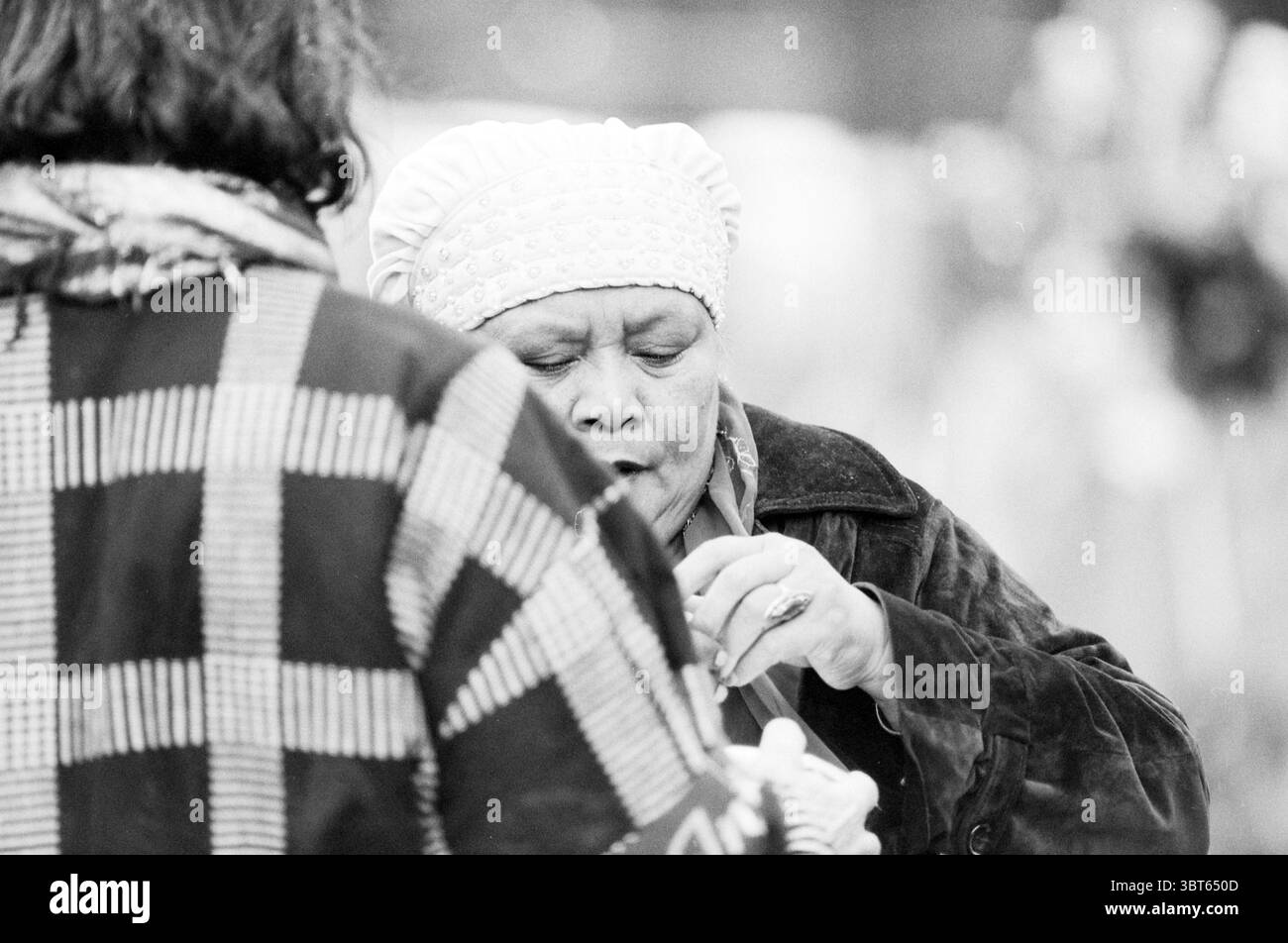 Tour silenzioso Bijlmer Amsterdam Paesi Bassi, Whizgle News, Dutch Desk, Paesi Bassi, 1950 - 2000 il 10-10-1992. Questi sono gli argomenti nell'immagine. La scena presenta due figure in un ambiente morbido e monocromatico, che evocano un senso di intimità e concentrazione. Una persona viene vista da dietro, vestita con un abito a motivi geometrici con un caratteristico design a scacchi, creando un netto contrasto con lo sfondo silenzioso. Il motivo a scacchi, con rendering in sfumature di grigio, aggiunge texture alla composizione complessiva. La seconda figura, posizionata in modo più prominente, indossa una copertura della testa di colore chiaro e una c scura Foto Stock