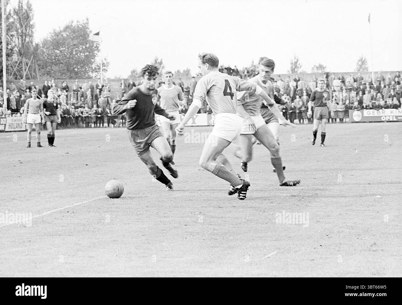 Partita di calcio Haarlem - ? Haarlem Jan Gijzenkade Paesi Bassi, Whizgle News, Dutch Desk, Paesi Bassi, 1950 - 2000 nel 1965. L'immagine include questi argomenti. La scena cattura un momento intenso su un campo di calcio, dove i giocatori sono impegnati in un gioco dinamico. A sinistra, un giocatore, vestito con una maglia scura, manovra abilmente la palla, mostrando agilità e concentrazione mentre si prepara a sfuggire ai suoi avversari. I colori contrastanti del suo vestito attirano l'attenzione sul suo movimento contro i toni più chiari del campo e dell'ambiente circostante. Intorno a lui ci sono tre giocatori avversari, identificabili da Foto Stock