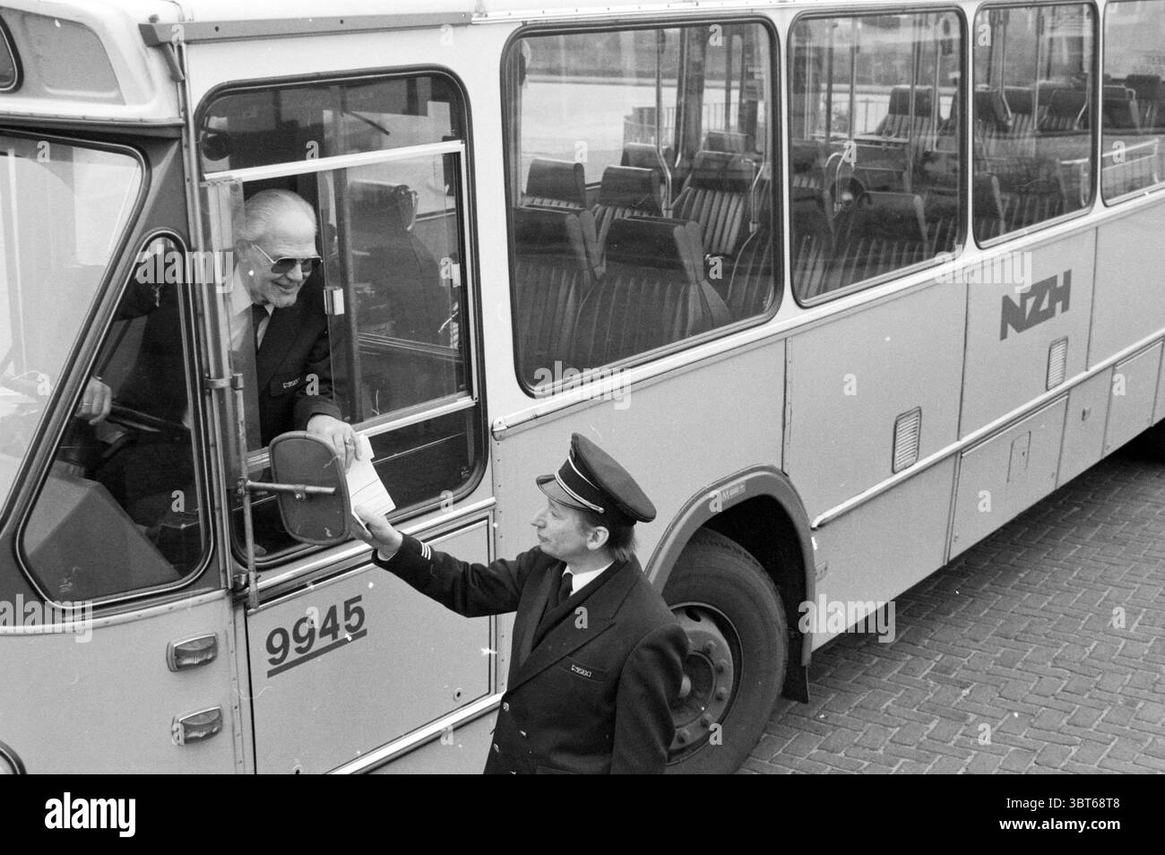 Varie foto all'interno e all'esterno dell'autobus NZH destinate alla pubblicità Noord Zuid Hollandse Vervoersmaatschappij N.V. NZ, Whizgle News, Dutch Desk, Paesi Bassi, 1950 - 2000 il 12-02-1987. Questi argomenti vengono visualizzati nell'immagine. In un vivace ambiente di trasporto, un autobus classico si erge in modo prominente, mostrando un esterno grigio argento che è sia nostalgico che funzionale. La parte anteriore del veicolo è dotata di un ampio parabrezza in cui due persone sono coinvolte in una conversazione. Una figura, vestita con una camicia bianca e occhiali da sole scuri, occupa il sedile del conducente, trasudando un'aria di autorità e professionalità. Foto Stock
