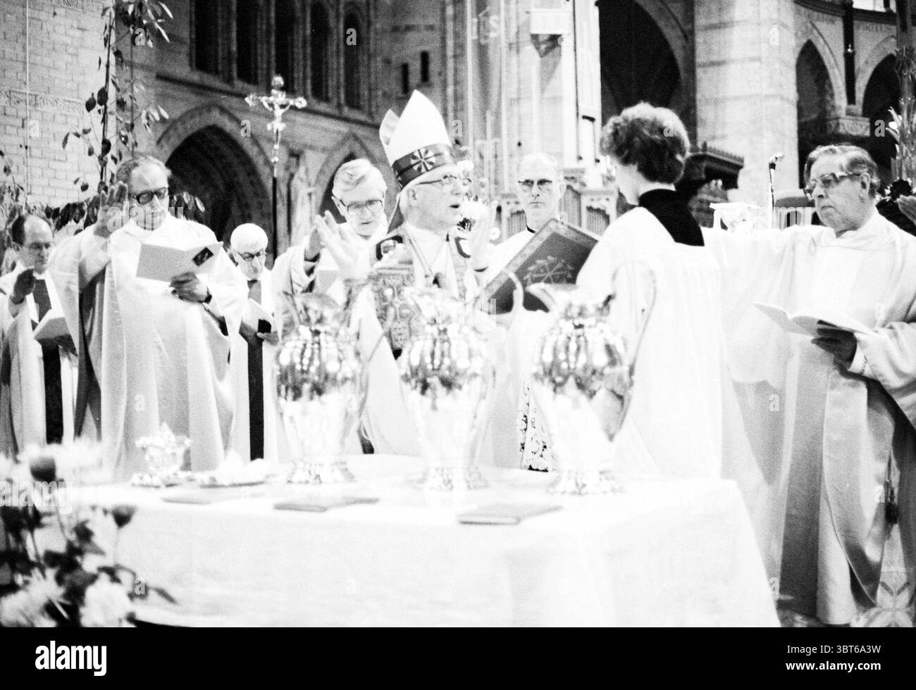 Consacrazione della Basilica del Santo olio, Chiese di Haarlem, Whizgle News, Dutch Desk, Paesi Bassi, 1950 - 2000 il 04-04-1980. L'immagine mostra questi argomenti. La scena si snoda all'interno di un grandioso e solenne interno, probabilmente una chiesa o una cattedrale, evidenziata da torreggianti colonne in pietra e intricati archi che raggiungono un soffitto a volta. L'atmosfera è intrisa di un senso di riverenza e tradizione. Diverse figure vestite in abiti religiosi formali si ergono in un semicerchio intorno a un altare splendidamente decorato, drappeggiato in un panno bianco. L'altare presenta navi d'argento scintillanti che catturano la sott Foto Stock