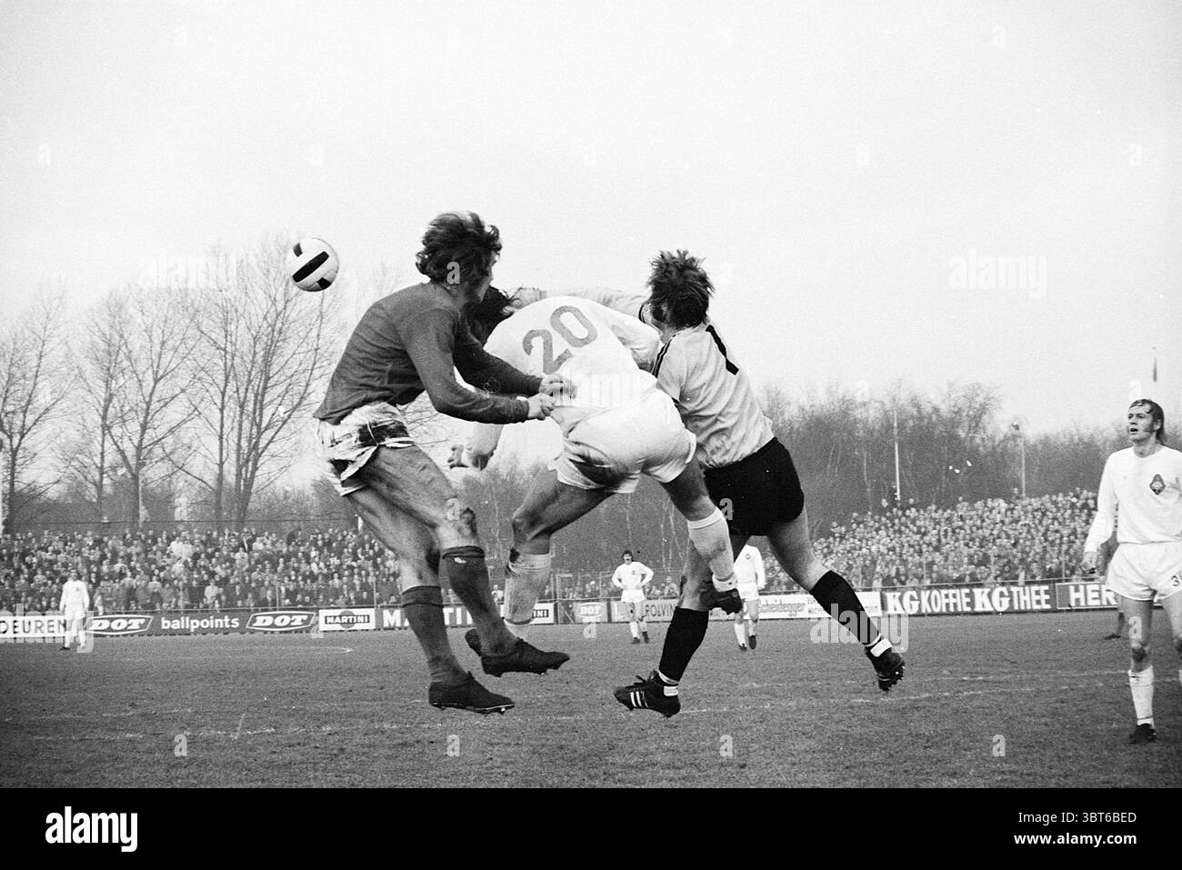 Partita di calcio Telstar contro AZ 67 Velsen., Whizgle News, Dutch Desk, Paesi Bassi, 1950 - 2000. L'immagine mostra questi argomenti. In una scena sportiva dinamica, due giocatori con uniformi contrastanti si impegnano in un momento intenso che circonda una palla da calcio aerea. Il giocatore in bianco, indossando il numero 20 ben visibile sulla schiena, salta alla testa della palla, il suo corpo si estende e si posiziona in un angolo che suggerisce determinazione e atleticità. I suoi capelli sono durati, indicando la natura fisica del gioco. Alla sua sinistra, un portiere, vestito con un'uniforme scura, si prepara per l'impen Foto Stock
