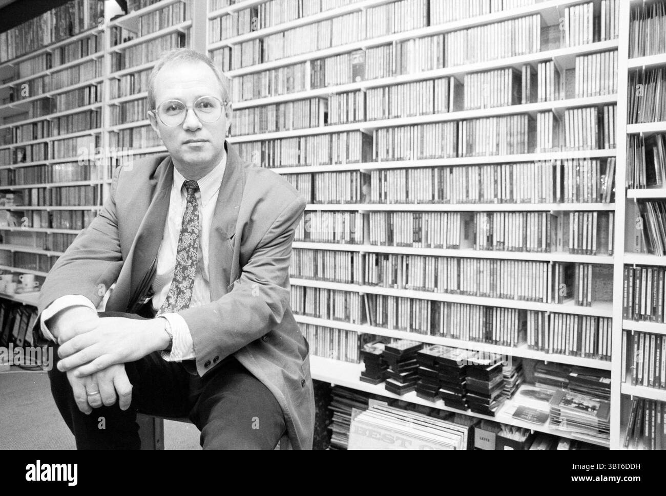 Mr. Paintbrush Sony Music, Whizgle News, Dutch Desk, Paesi Bassi, 1950 - 2000 on 25-04-1991. Questi argomenti sono mostrati nell'immagine. La scena presenta una seduta individuale ben vestita in una posa rilassata, trasuda un'aria di raffinatezza. Ha capelli corti e chiari e indossa occhiali rotondi che gli conferiscono un aspetto intellettuale. Il suo abito è un tono tenue, completato da una cravatta a motivi geometrici che aggiunge un tocco di colore. Sullo sfondo, c'è un muro torreggiante pieno di scaffali ben disposti, traboccanti di numerosi CD, che suggeriscono una collezione musicale ampia e diversificata. Il Foto Stock