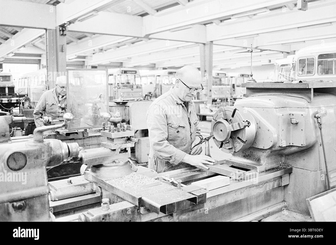 Rapporto N.Z.H. Noord Zuid Hollandse Vervoersmaatschappij N.V. NZ, Whizgle News, Dutch Desk, Paesi Bassi, 1950 - 2000 il 14-11-1967. Questi sono gli argomenti nell'immagine. La scena si sviluppa all'interno di un grande spazio di lavoro industriale, caratterizzato da alti soffitti e corridoi spaziosi pieni di vari macchinari. L'aria è vibrante con un'atmosfera di produttività e scopo. In primo piano, un uomo, vestito con un'uniforme da lavoro, è concentrato su un intricato tornio metallico. La sua concentrazione suggerisce un impegno profondo con il compito in questione, mentre manipola con cura un pezzo di materiale che viene modellato Foto Stock