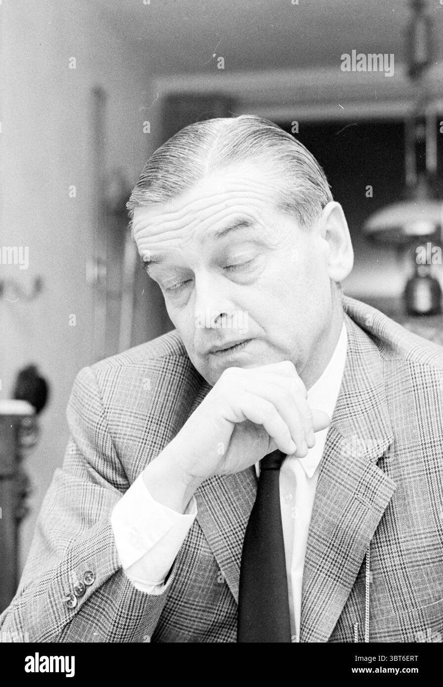 Van Randwijk Noord Zuid Hollandse Vervoersmaatschappij N.V. NZ, Whizgle News, Dutch Desk, Paesi Bassi, 1950 - 2000 il 18-02-1971. L'immagine mostra questi argomenti. Un uomo di mezza età è seduto a un tavolo, trasuda un umore contemplativo. La sua pelle è leale e i suoi capelli grigi e dalla schiena affilata aggiungono un'aria di raffinatezza. È vestito con un abito a scacchi con una camicia bianca sotto e una cravatta scura, suggerendo un ambiente formale. La sua espressione è premurosa, con gli occhi parzialmente chiusi, come se fosse profondamente riflesso o considerasse un'idea complessa. Appoggia il mento sulla mano, aggiungendo alla penna Foto Stock