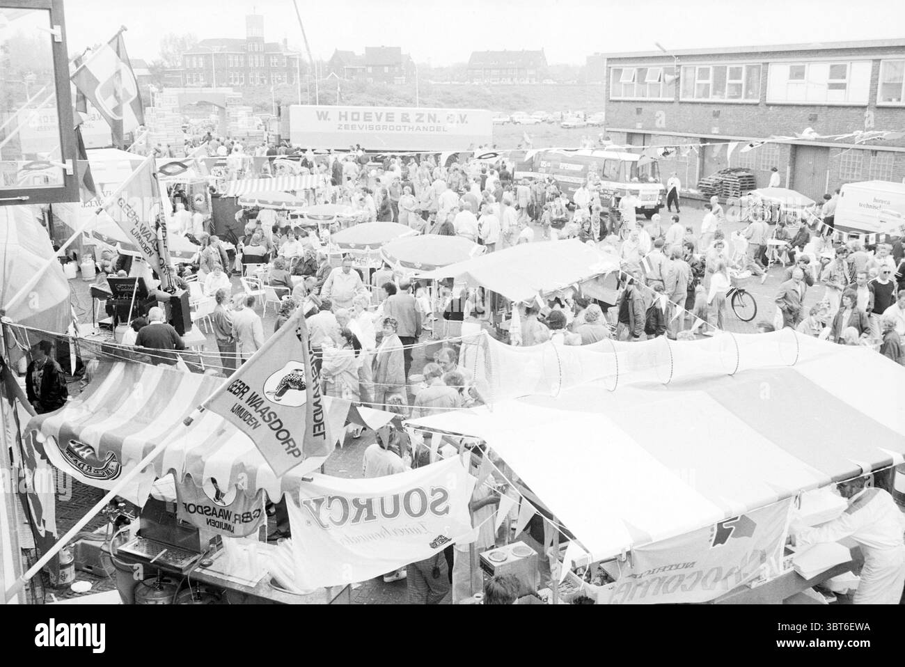Giornata della pesca IJmuiden pesca e altri pescivendoli pesca IJmuiden Paesi Bassi, Whizgle News, Dutch Desk, Paesi Bassi, 1950 - 2000 il 16-06-1987. Questi sono gli elementi dell'immagine. La scena cattura un vivace evento all'aperto, probabilmente un mercato o un festival, con una folta folla di persone riunite insieme. Molti individui sono vestiti con abiti di colore chiaro, suggerendo un'atmosfera informale, forse calda. Più bancarelle occupano l'area, ognuna coperta da tende da sole in varie tonalità di bianco e colori pastello, creando un effetto patchwork sopra la testa. Alcune bancarelle mostrano bandiere colorate e. Foto Stock
