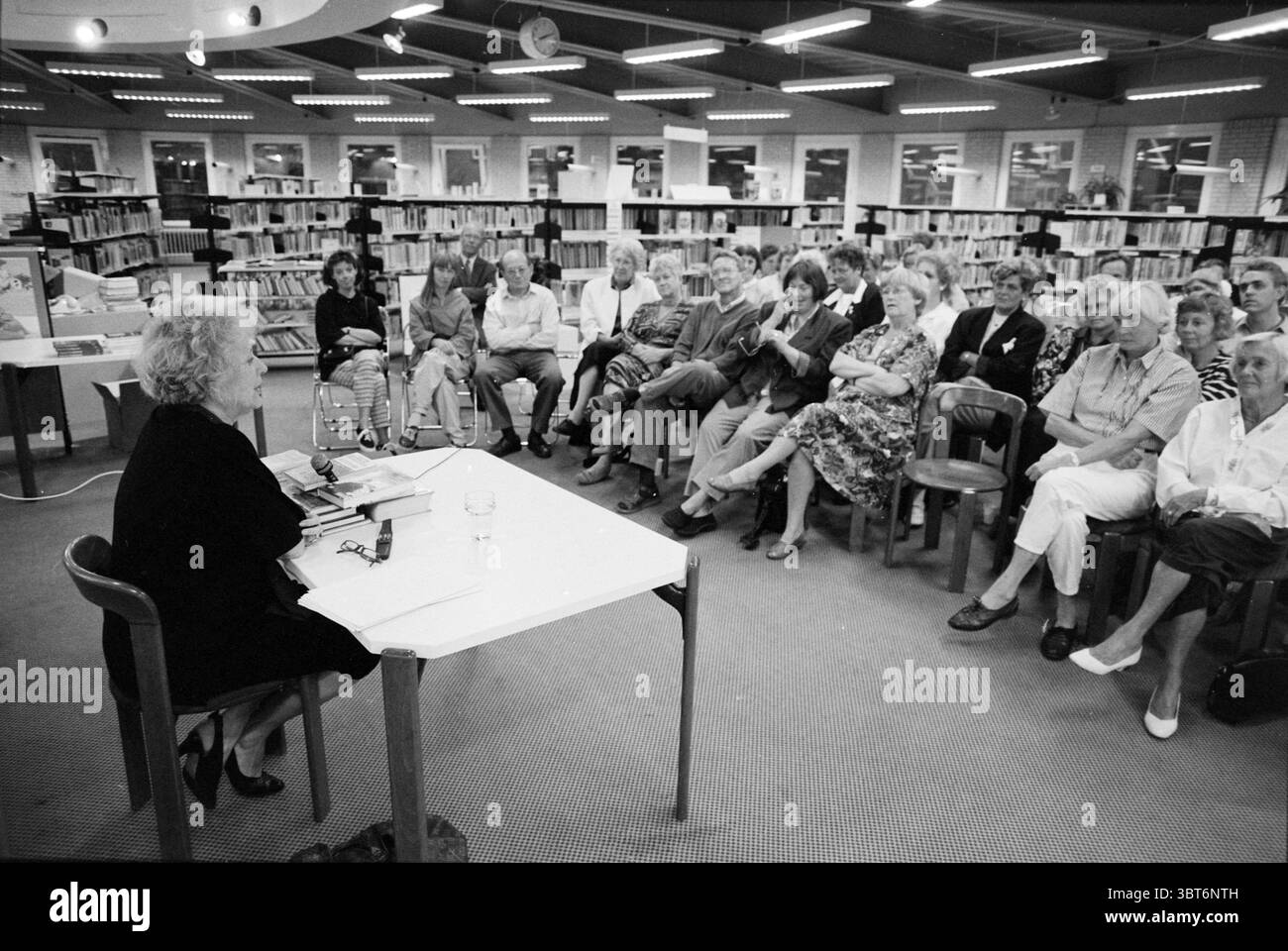 M.Best lecture Noordwijkerhout Noordwijkerhout, Whizgle News, Dutch Desk, Paesi Bassi, 1950 - 2000 il 12-09-1990. Questi sono gli argomenti nell'immagine. La scena ritrae un raduno in una biblioteca, dove uno speaker è posizionato ad un tavolo di fronte al pubblico. L'oratrice, una donna, siede in prima linea, circondato da diverse pile di libri. La sua espressione suggerisce coinvolgimento ed entusiasmo quando si rivolge al gruppo. Il pubblico comprende un diverso mix di individui, tra cui uomini e donne di varie età. Sono seduti su sedie di legno, con attenzione all'altoparlante. Un po' di atte Foto Stock