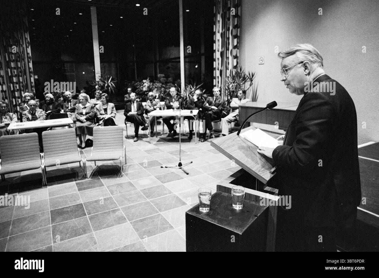 Intervento del sig. Ginjaar VVD incontro con il municipio Heemstede V.V.D. Heemstede Paesi Bassi, Whizgle News, Dutch Desk, Paesi Bassi, 1950 - 2000 il 21-03-1989. L'immagine include questi argomenti. In una spaziosa sala, l'atmosfera è piena di un senso di riverenza e attenzione. In prima linea, un oratore si trova su un podio di legno, profondamente impegnato a tenere un discorso. Il suo abbigliamento è formale, con una tuta scura che contrasta con le calde tonalità del legno del podio. I suoi capelli vengono pettinati con cura e tiene alcuni fogli di carta in una mano mentre gestiva con l'altra, sottolineando il suo Foto Stock