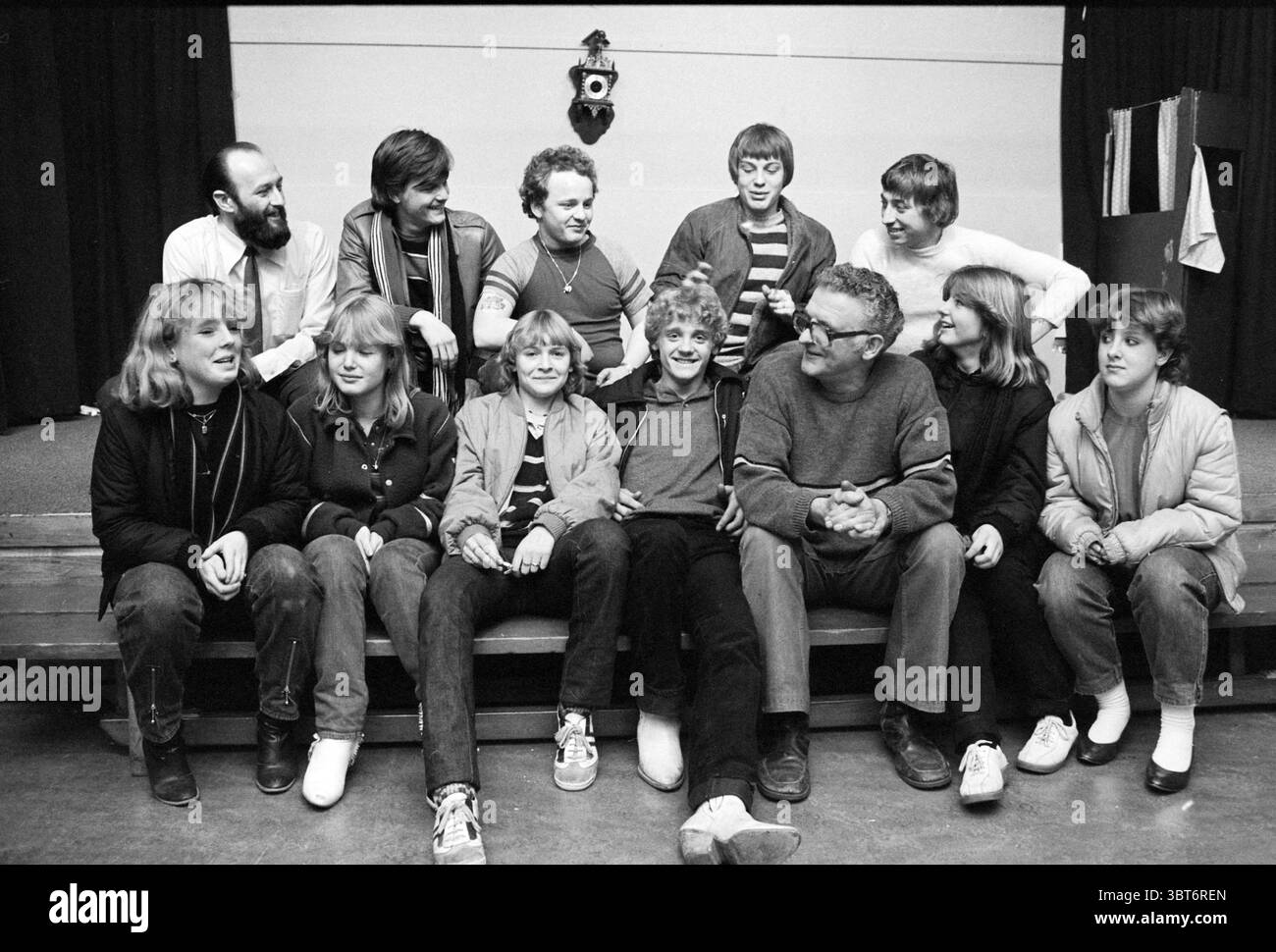 Gruppo giovanile quartiere indiano Haarlem gruppi Gioventù e giochi giovanili Haarlem Paesi Bassi, Whizgle News, Dutch Desk, Paesi Bassi, 1950 - 2000 il 17-02-1981. Questi sono gli elementi dell'immagine. La scena raffigura un raduno di un grande gruppo di persone sedute su una panchina di legno, disposte in modo informale e organizzato. Ci sono otto persone in primo piano e molte altre sullo sfondo, ognuna con un distinto senso di personalità e cameratismo. Lo sfondo è un palcoscenico semplice e poco illuminato con tende nere che si avvolgono verso il basso, offrendo un contrasto con i toni più chiari della fr Foto Stock Gruppo giovanile quartiere indiano Haarlem gruppi Gioventù e giochi giovanili Haarlem Paesi Bassi, Whizgle News, Dutch Desk, Paesi Bassi, 1950 - 2000 il 17-02-1981. Questi sono gli elementi dell'immagine. La scena raffigura un raduno di un grande gruppo di persone sedute su una panchina di legno, disposte in modo informale e organizzato. Ci sono otto persone in primo piano e molte altre sullo sfondo, ognuna con un distinto senso di personalità e cameratismo. Lo sfondo è un palcoscenico semplice e poco illuminato con tende nere che si avvolgono verso il basso, offrendo un contrasto con i toni più chiari della fr Foto Stock