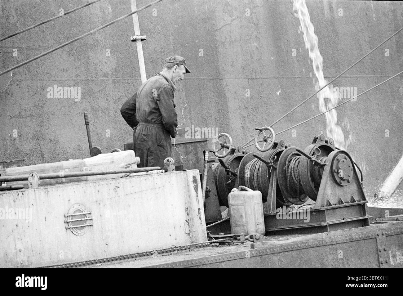 Equipaggi di salvataggio a Wan Chun Alderman, Whizgle News, Dutch Desk, Paesi Bassi, 1950 - 2000 il 21-09-1973. Questi argomenti sono mostrati nell'immagine. La scena cattura una figura, un uomo più anziano, vestito con abiti da lavoro oscuri, probabilmente una tuta, in piedi vicino a una complessa disposizione di macchinari su una nave. La sua postura suggerisce la concentrazione, mentre lui tende al compito che sta svolgendo. Il macchinario è costituito da diversi grandi bobine circolari, ordinatamente disposte in linea, che appaiono un po' intemperie e industriali, suggerendo un ambiente marittimo esigente. Lo sfondo presenta una superficie ruvida dello scafo di una nave, Foto Stock