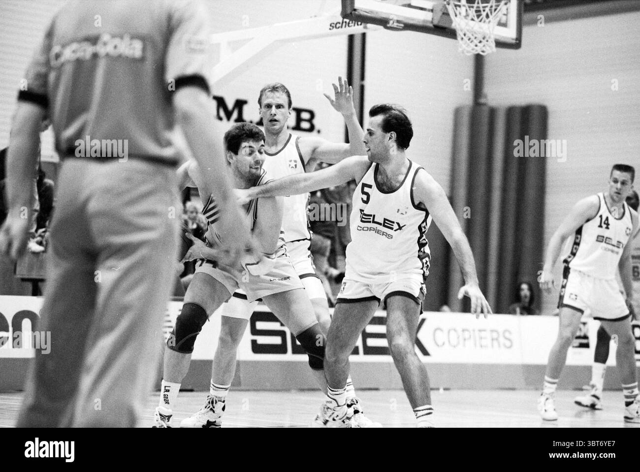 Akrides week Haarlem Paesi Bassi, Whizgle News, Dutch Desk, Paesi Bassi, 1950 - 2000 il 07-04-1992. Questi sono gli argomenti nell'immagine. La scena cattura un momento intenso da una partita di basket. Un gruppo di giocatori è impegnato sul campo, mostrando uno spettro di atletismo e strategia. In primo piano, due atleti sono bloccati in una gara per il posizionamento. Uno, vestito con un'uniforme scura, sembra che stia tentando di guidare verso il cesto, il suo corpo basso e pronto per una manovra. L'altro giocatore, indossando una maglia bianca impreziosita da un numero, è fermo, pronto a difendersi Foto Stock