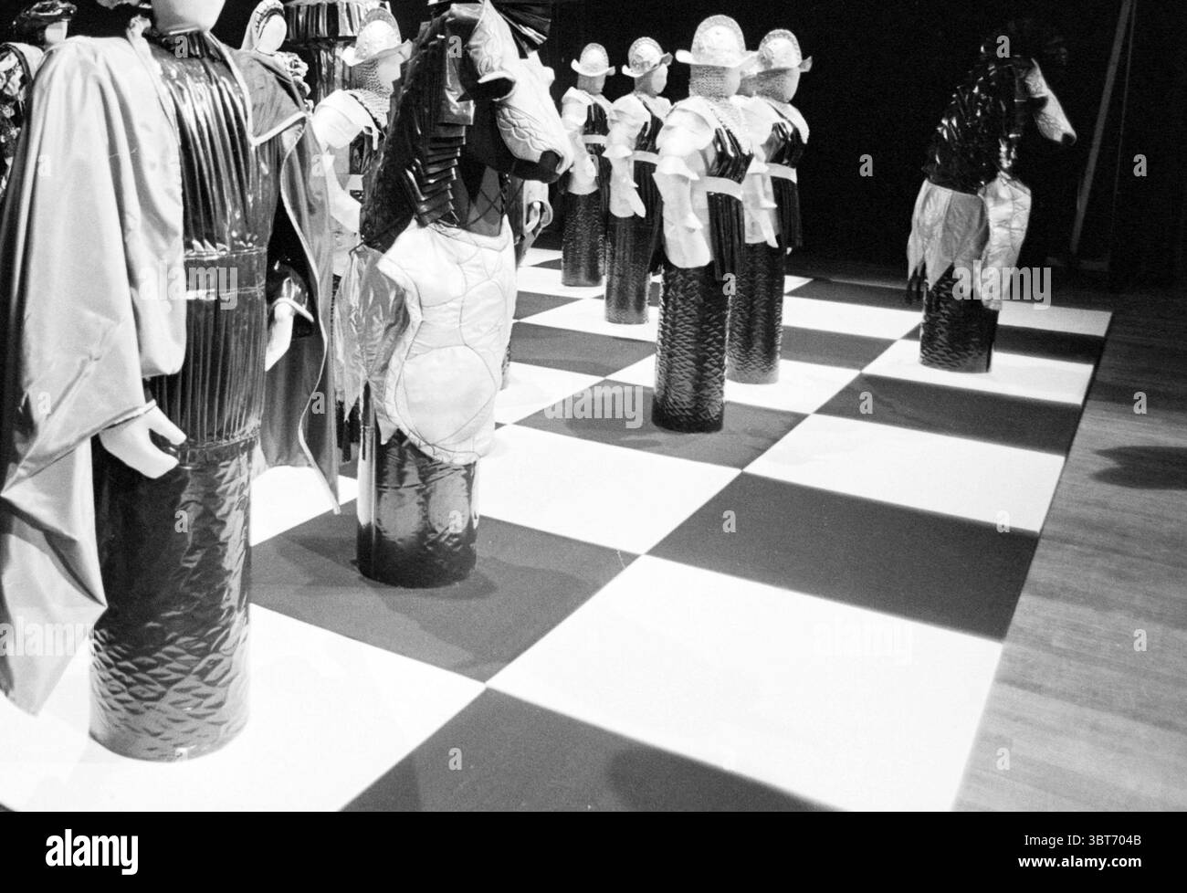 Apertura e sorteggio HST Beverwijk Blast Furnace Chess Tournament Wijk aan Zee, Whizgle News, Dutch Desk, Paesi Bassi, 1950 - 2000 il 17-01-1985. Questi sono gli argomenti nell'immagine. La scena presenta un'ampia scacchiera che si estende su tutto il terreno, con un sorprendente motivo a scacchi bianco e nero. Ogni quadrato si alterna tra nero intenso e bianco brillante, creando un contrasto audace. Torreggianti sopra il tabellone sono pezzi da scacchi dal design unico che ricordano figure vestite con costumi elaborati. Su un lato, i pezzi sono decorati con un abbigliamento simile a un'armatura, completo di decorazioni metalliche Foto Stock
