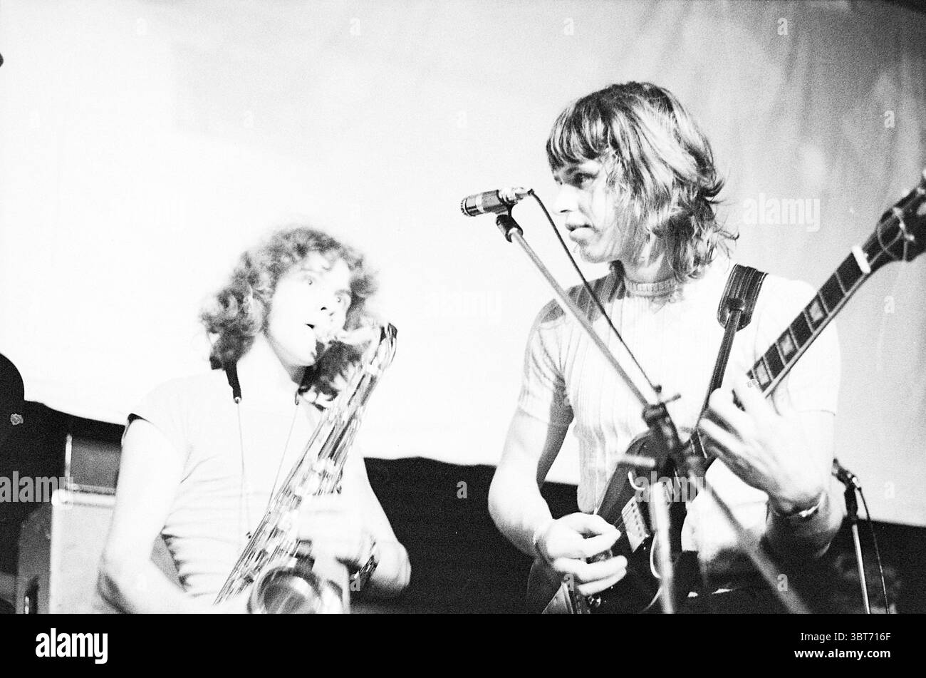 Esibizione dei Cats della Dizzy Man's Band e di altri artisti e gruppi. Music, Whizgle News, Dutch Desk, Paesi Bassi, 1950 - 2000 on 26-11-1970. L'immagine include questi argomenti. Nella scena, due musicisti si esibiscono sul palco sotto una luce soffusa e ambientale che proietta un caldo bagliore sulle loro figure. L'ambiente suggerisce un'atmosfera intima da concerto, probabilmente in un piccolo locale, con uno sfondo scuro che contrasta con la zona più luminosa del palco. Un musicista, posizionato leggermente a sinistra, suona uno strumento di ottone. Ha capelli ricci e voluminosi e trasuda entusiasmo, appoggiandosi al suo istr Foto Stock