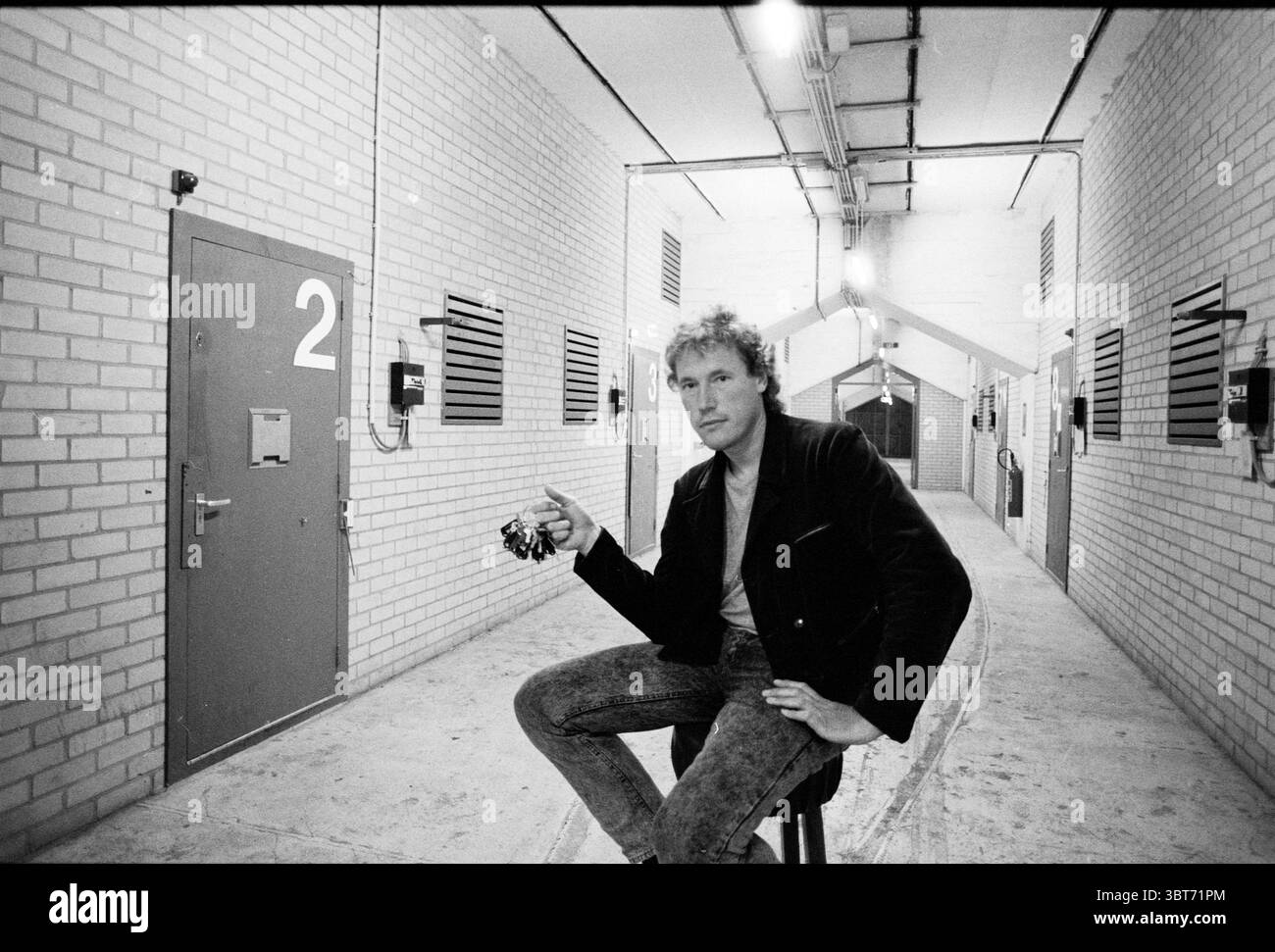 Sig. Scheeps in POP bunker IJmuiden Persons IJmuiden Paesi Bassi, Whizgle News, Dutch Desk, Paesi Bassi, 1950 - 2000 il 26-08-1988. Questi argomenti vengono visualizzati nell'immagine. La scena si sviluppa in un corridoio rigido caratterizzato da pareti lisce e chiare in mattoni. Il pavimento, una lastra di cemento, aggiunge un tocco industriale. L'illuminazione è luminosa ma morbida, illuminando lo spazio senza ombre dure, creando un'atmosfera neutra che favorisce la messa a fuoco e l'introspezione. A sinistra, si distingue una porta contrassegnata con il numero "2", la cui superficie metallica riflette leggermente la luce ambientale. Lungo il corridoio, ci sono Foto Stock