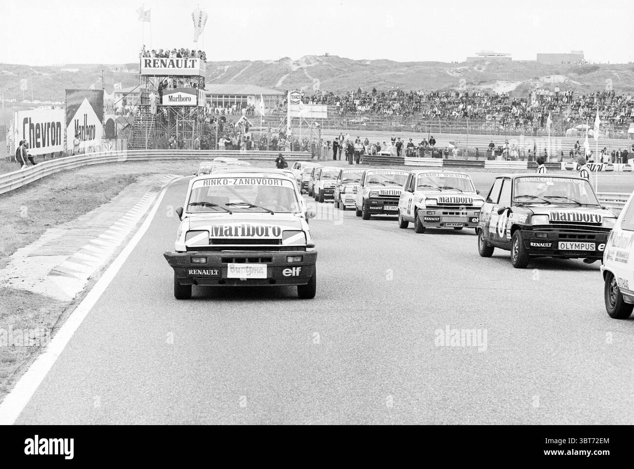 Renault Race Zandvoort Renault Zandvoort, Whizgle News, Dutch Desk, Paesi Bassi, 1950 - 2000 il 25-05-1980. L'immagine include questi argomenti. La scena è ambientata su un circuito, dove una serie di piccole auto si muove in formazione, trasudando energia ed eccitazione. In prima linea, un'auto è in testa al gruppo, contraddistinta da una grafica di sponsorizzazione. Il design dei veicoli varia, mostrando colori diversi, anche se il tono generale è attenuato, inclinato verso il bianco e il nero. Sullo sfondo, è visibile una folla, che si riunisce in tribune che si innalzano sopra la pista. Il pubblico appare animato, thei Foto Stock