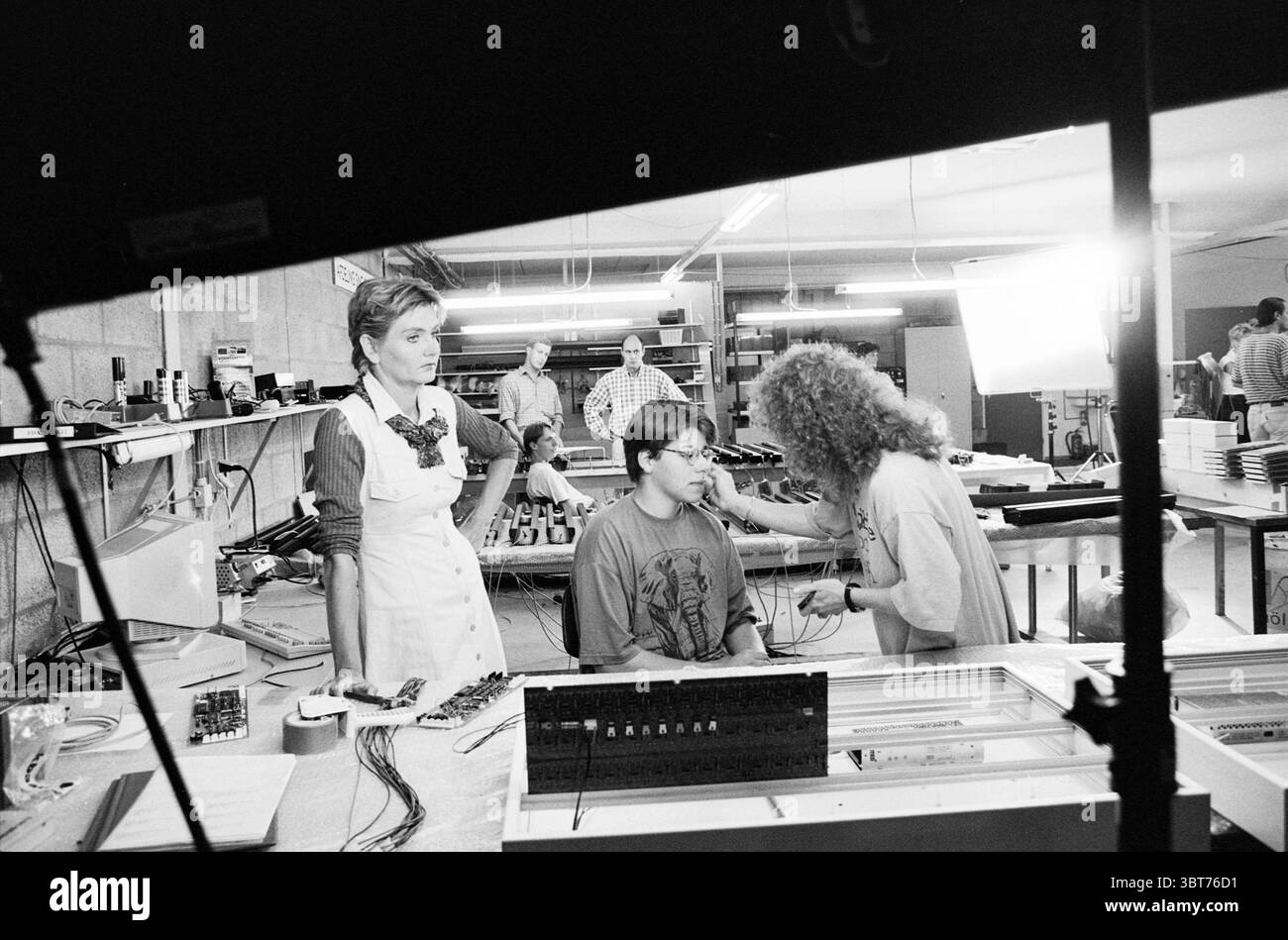 Registrazione su pellicola) fa. Surtronic Waarderpolder, Whizgle News, Dutch Desk, Paesi Bassi, 1950 - 2000 il 31-07-1995. Questi argomenti sono mostrati nell'immagine. In uno spazio di lavoro vivace, i singoli individui sono impegnati in varie attività relative all'elettronica e all'assemblaggio. La scena ha un'estetica monocromatica che le conferisce una qualità senza tempo. In primo piano, un adolescente con capelli corti e occhiali si siede a un tavolo, focalizzato su un compito che viene eseguito sul suo viso da un individuo con capelli ricci. Questa persona è adornata da un abito casual, che suggerisce un ambiente pratico. L'interazione sembra intima e c Foto Stock