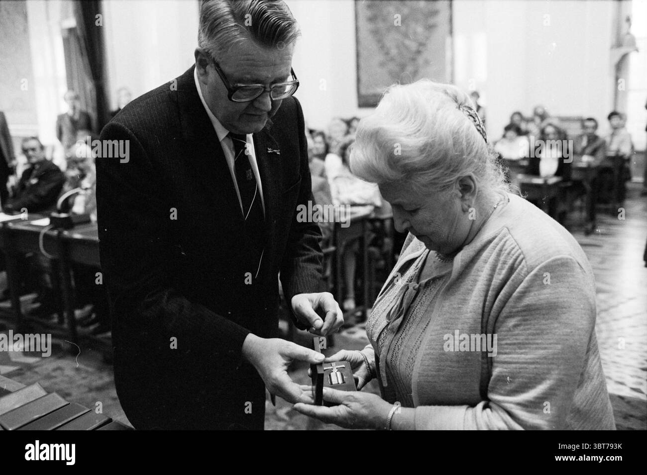 Presentazione delle croci di resistenza da parte del Commissario della Regina Roel de WIT nella Casa Prov. Stati Prov. Water Management Provincial House Haarlem Paesi Bassi, Whizgle News, Dutch Desk, Paesi Bassi, 1950 - 2000 il 21-01-1982. Questi sono gli argomenti nell'immagine. In un ambiente interno formale, la scena è caratterizzata da un senso di cerimonia e riconoscimento. L'attenzione è rivolta a due individui in primo piano: Un uomo e una donna impegnati in un momento significativo. L'uomo, vestito con un abito scuro e con gli occhiali, ha un comportamento che trasuda autorità e rispetto. E' posizionato a fessura Foto Stock