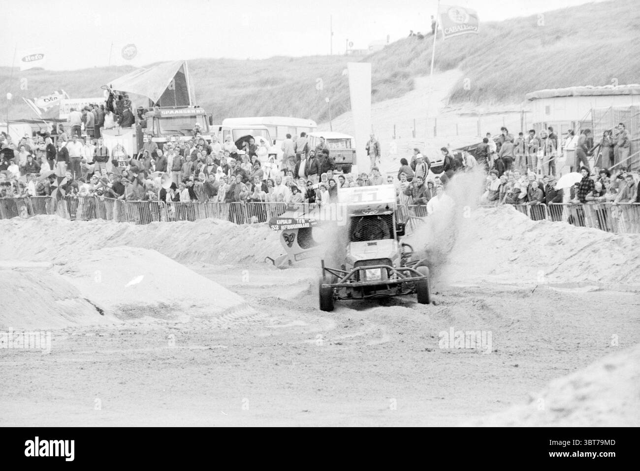 Strandcross Wijk aan Zee Beach and Beaches Wijk aan Zee, Whizgle News, Dutch Desk, Paesi Bassi, 1950 - 2000 on 27-09-1987. Questi sono gli argomenti nell'immagine. La scena cattura un evento esilarante che si svolge su un terreno sabbioso, probabilmente una spiaggia o una zona costiera. C'è un senso di eccitazione nell'aria, mentre una folla di spettatori si riunisce lungo un'area recintata, con i loro volti pieni di attesa. In primo piano, un robusto veicolo fuoristrada corre attraverso il terreno sabbioso, gettando una nuvola di polvere e particelle di sabbia. Il veicolo è progettato per offrire prestazioni elevate, con un telaio robusto e. Foto Stock