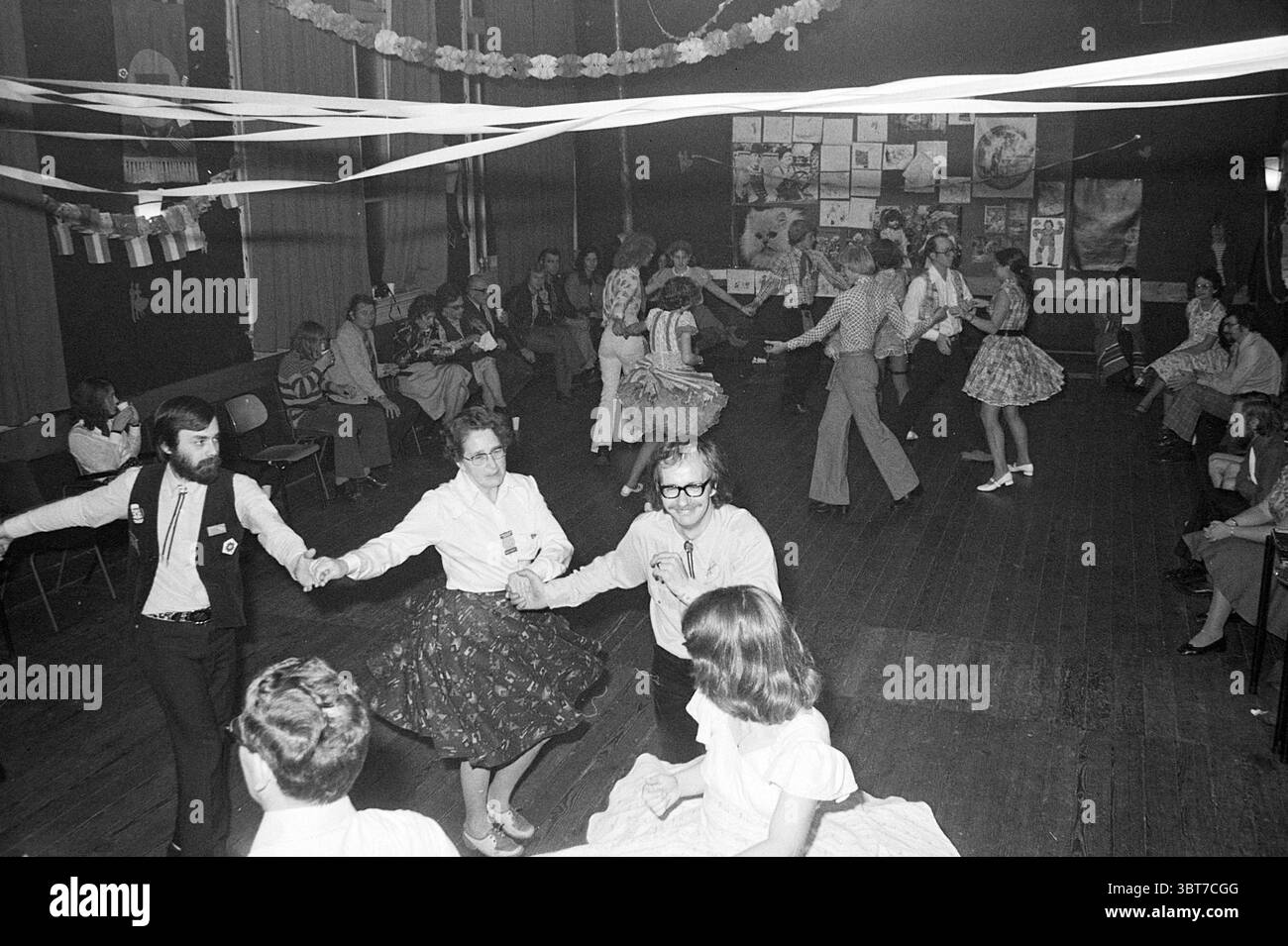 Ballo di piazza "de Deining" a Haarlem Dancing, Whizgle News, Dutch Desk, Paesi Bassi, 1950 - 2000 on 25-10-1975. Questi argomenti vengono visualizzati nell'immagine. In un ambiente interno vivace, un gruppo di persone è impegnato in una danza gioiosa. Lo spazio è caratterizzato da un pavimento rustico in legno che esalta l'atmosfera calda e nostalgica. I partecipanti, vestiti con abiti vivaci della metà del XX secolo, aggiungono spruzzi di colore alla scena. Le donne indossano abiti con gonne svasate e motivi floreali, mentre alcune hanno i loro capelli con onde retrò. Gli uomini si vedono in camicie e pantaloni, con qualche spor Foto Stock