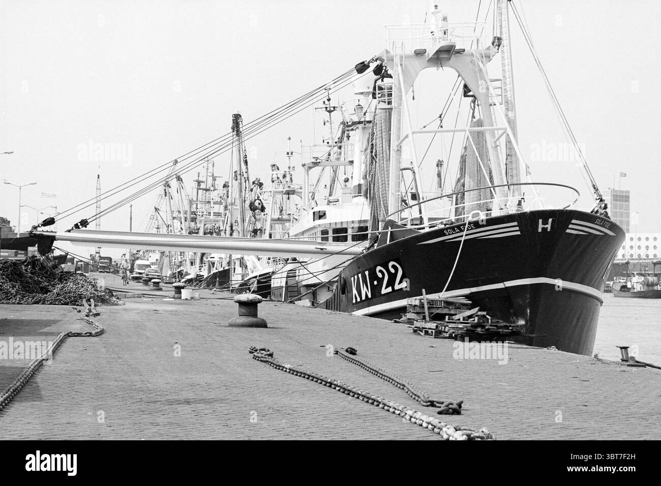Banchina da traino con navi IJmuiden IJmuiden Trawlerkade Paesi Bassi, Whizgle News, Dutch Desk, Paesi Bassi, 1950 - 2000 il 07-08-1996. L'immagine mostra questi argomenti. In una vivace scena portuale, un grande peschereccio domina il primo piano, il suo scafo dipinto in nero intenso con audaci scritte bianche che ne segnano la designazione. La struttura è robusta, con un ponte alto e un albero esteso che raggiunge il cielo. Intorno a questa nave, molte altre navi punteggiano il porto, alcune più grandi e industriali, mentre altre appaiono più modeste nelle dimensioni, tutte ancorate in linee pulite. Il dock è pa Foto Stock