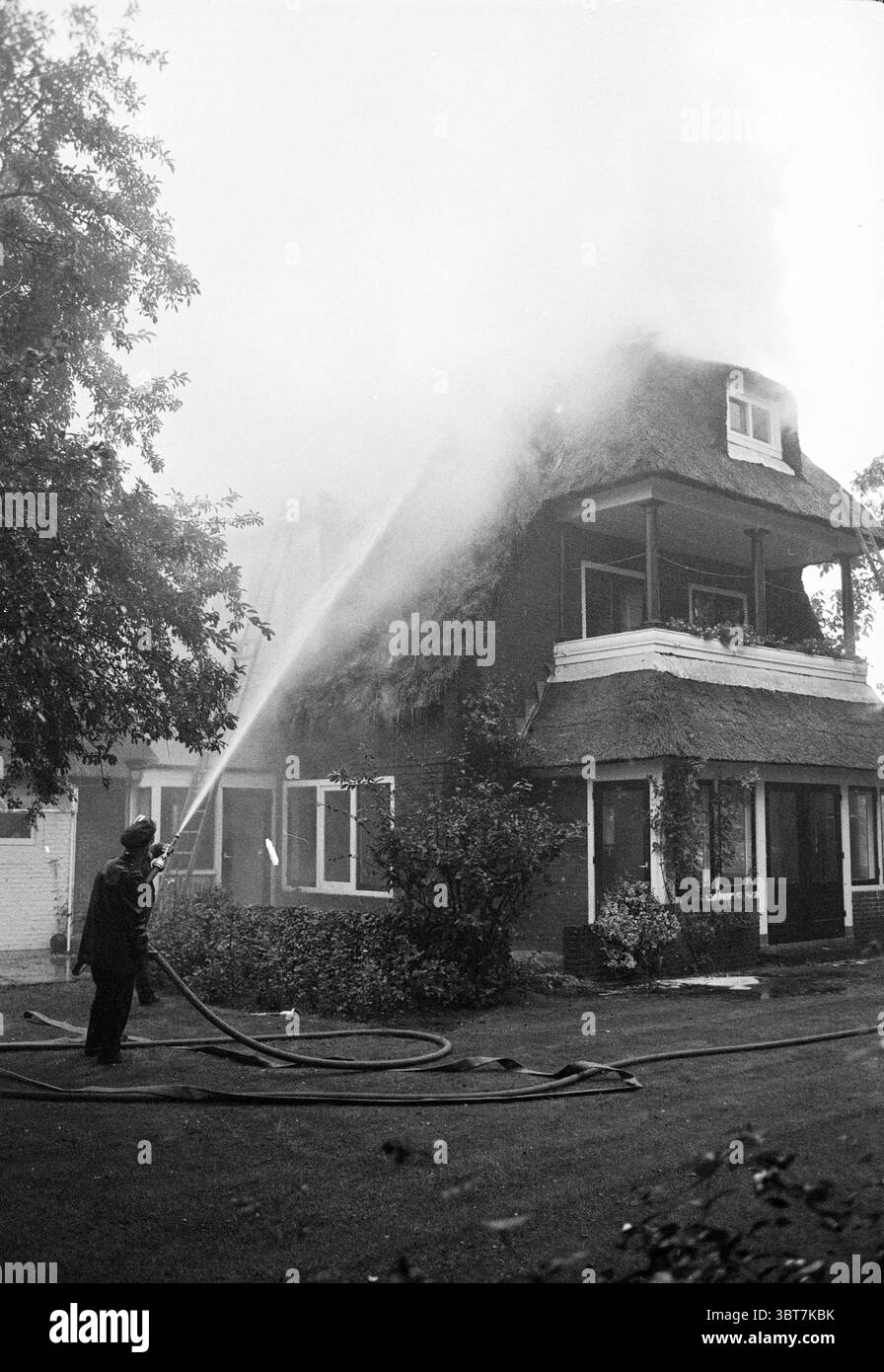 Vigili del fuoco Aerdenhout, vigili del fuoco, Whizgle News, Dutch Desk, Paesi Bassi, 1950 - 2000 il 17-09-1969. L'immagine contiene questi argomenti. In una scena drammatica, una casa è sommersa da un denso pennacchio di fumo, che fuoriesce dalle sezioni superiori della struttura. L'abitazione presenta un caratteristico tetto in paglia che le conferisce un fascino rustico, ma la situazione attuale contrasta nettamente con il suo aspetto caratteristico. Le pareti sono dipinte con un'ombra scura, possibilmente marrone o rosso profondo, con finiture bianche intorno alle finestre che aggiungono una decorazione sottile. Un vigile del fuoco, rivestito di equipaggiamento protettivo, sta sulla gro Foto Stock