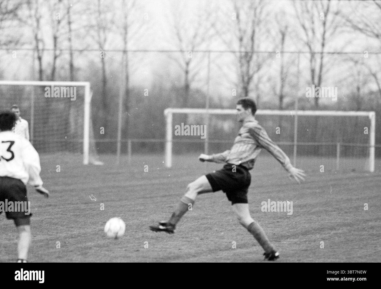Sizo - KHFC, Whizgle News, Dutch Desk, Paesi Bassi, 1950 - 2000 il 18-11-1994. Questi argomenti vengono visualizzati nell'immagine. In un ambiente vivace all'aperto, due giocatori sono impegnati in una partita di calcio su un campo erboso. In primo piano un giocatore, rivestito di maglia a strisce e pantaloncini scuri, esegue abilmente un calcio verso la palla, che si trova proprio di fronte a lui. La sua postura è atletica e dinamica, suggerendo concentrazione e determinazione mentre si prepara allo sciopero. Un altro giocatore, vestito con una maglia bianca con pantaloncini scuri, si trova nelle vicinanze, osservando il gioco. Il suo linguaggio del corpo indica readi Foto Stock