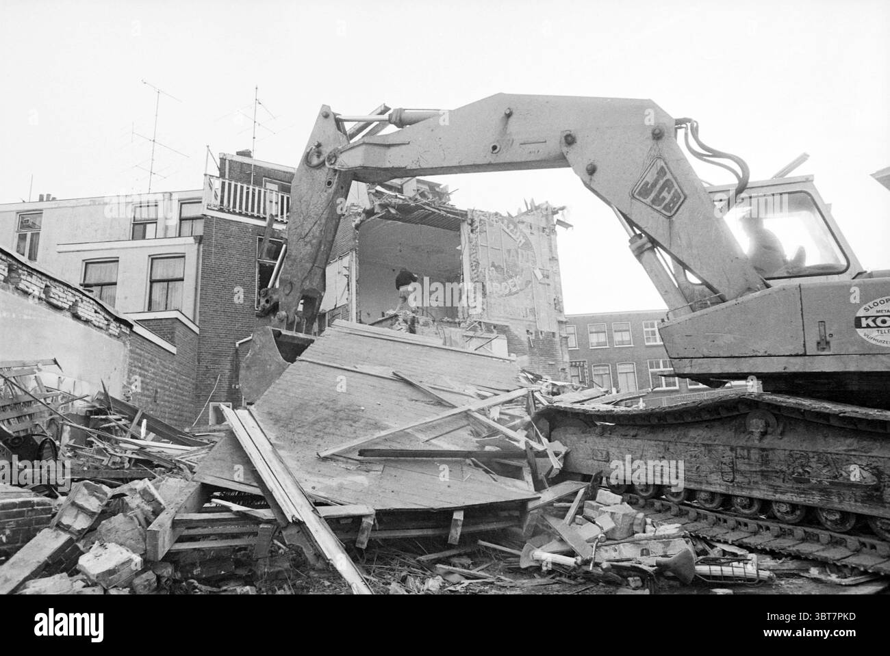 Edificio demolizione Wagenpand Schouwtjeslaan demolizione demolizione cantieri Haarlem Wagenweg Paesi Bassi, Whizgle News, Dutch Desk, Paesi Bassi, 1950 - 2000 il 08-11-1978. L'immagine contiene questi argomenti. La scena raffigura un cantiere segnato dalla distruzione. Una grande e pesante macchina da scavo domina il primo piano, il suo braccio metallico si estende mentre separa i resti di un edificio. Polvere e detriti si diffondono nel terreno, formando una miscela caotica di mattoni frantumati e legname. Sullo sfondo si erge il profilo di un altro edificio, parzialmente intatto ma in netto contrasto Foto Stock