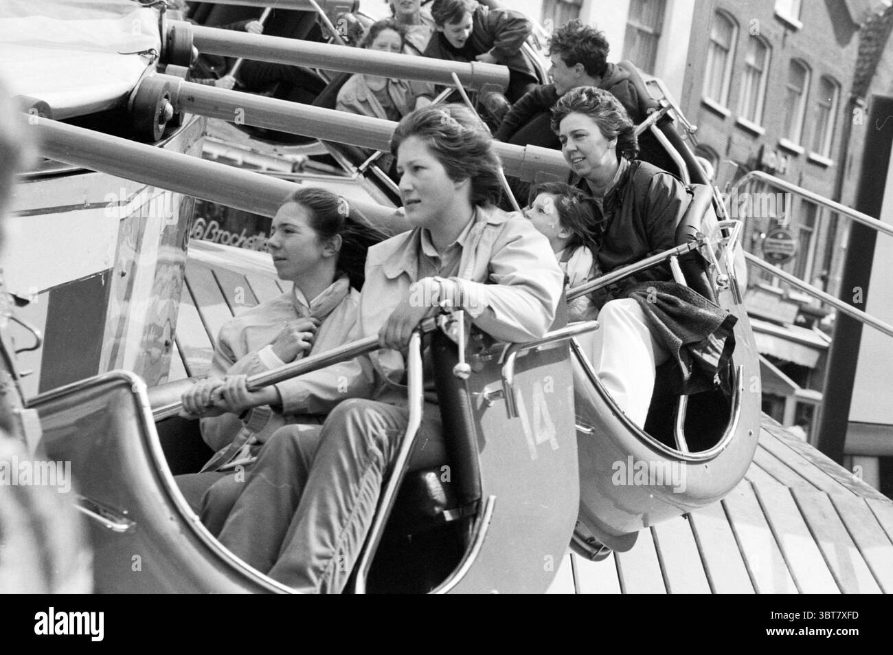 Fair Queen's Day, Whizgle News, Dutch Desk, Paesi Bassi, 1950 - 2000 il 30-04-1983. Questi sono gli argomenti nell'immagine. La scena cattura un vivace giro di divertimento in movimento, con un gruppo di quattro donne sedute in un piccolo veicolo chiuso che fa parte di un'attrazione rotante. Ogni donna mostra un mix di espressioni; alcune sembrano ridere, mentre altre mostrano sorpresa o eccitazione. I loro capelli sono infastiditi dal movimento, aumentando il senso di emozione. La tavolozza dei colori è prevalentemente monocromatica e presenta sfumature di grigio che trasmettono un senso di nostalgia. Le donne sono vestite Foto Stock