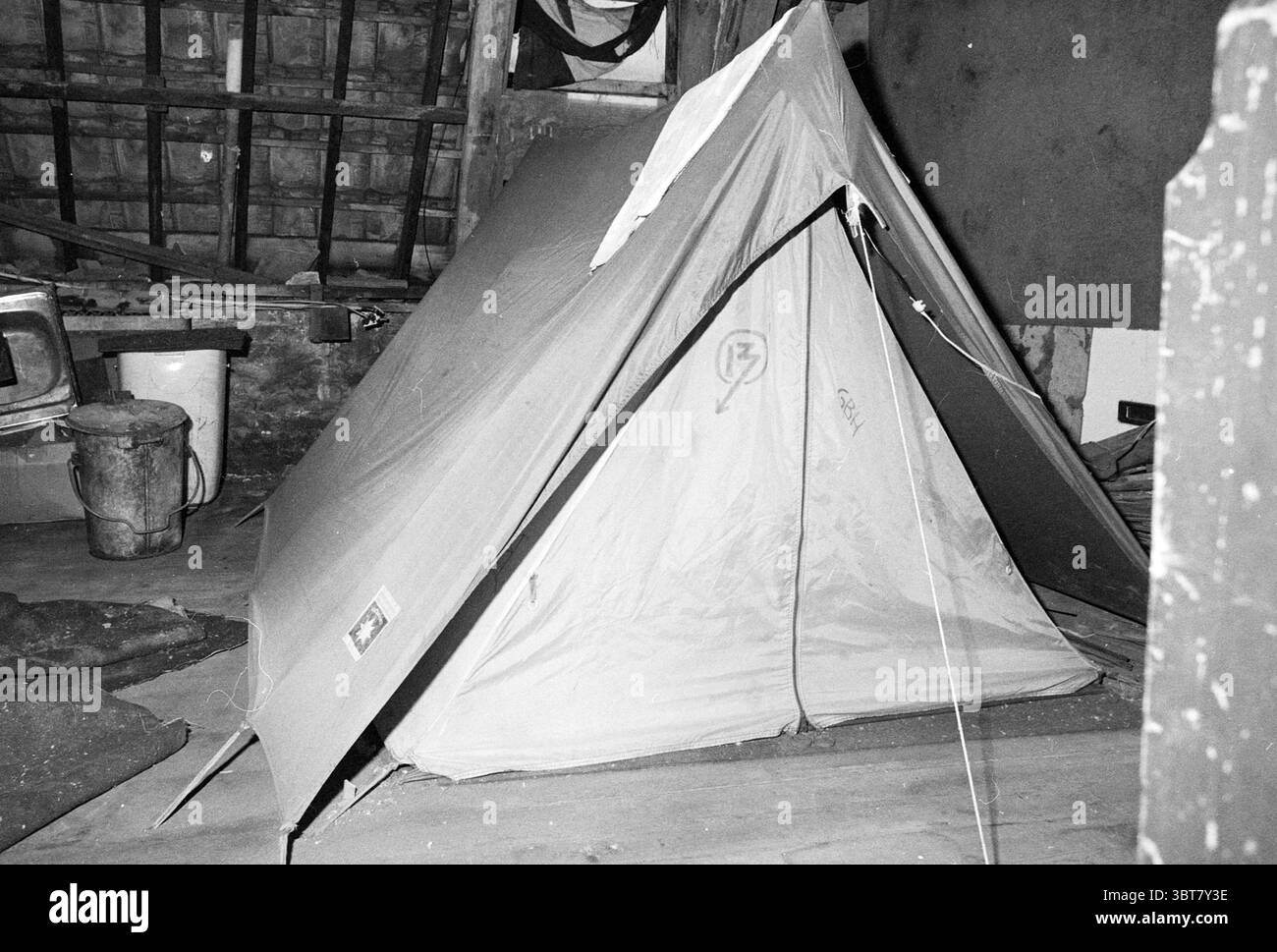 Edificio squatter nell'ex stazione di polizia di Jansweg Kraken Haarlem Jansweg Paesi Bassi, Whizgle News, Dutch Desk, Paesi Bassi, 1950 - 2000 il 05-01-1983. Questi sono gli elementi dell'immagine. La scena presenta una tenda collocata in modo prominente in uno spazio interno ingombrante e poco illuminato. La tenda è di forma triangolare, con un tessuto beige che appare leggermente usurato e piegato, suggerendo che abbia visto un certo uso. Il suo ingresso è parzialmente zippato, consentendo un'occhiata all'ombra interna. Intorno alla tenda è presente un assortimento di oggetti che conferiscono allo spazio un aspetto robusto e vivibile. Il pavimento lo è Foto Stock