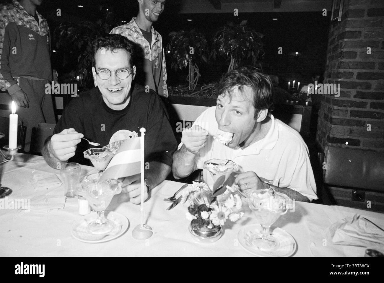 Due giocatori di pallamano Akersloot Akersloot, Whizgle News, Dutch Desk, Paesi Bassi, 1950 - 2000 il 21-11-1994. L'immagine mostra questi argomenti. La scena cattura un ambiente vivace del ristorante, pieno di un'atmosfera calda e invitante. Due uomini siedono a un tavolo, ciascuno gustando un grande dessert servito in eleganti ciotole di vetro. Le ciotole sono traboccanti di gelati e ricoperte di vari deliziosi garnici. Un uomo, che indossa occhiali e una camicia scura, sorride molto mentre tiene in mano un cucchiaio pronto a prendere un altro morso della sua sorpresa. La sua espressione trasmette gioia e soddisfazione. L'altro uomo, in un shi bianco Foto Stock