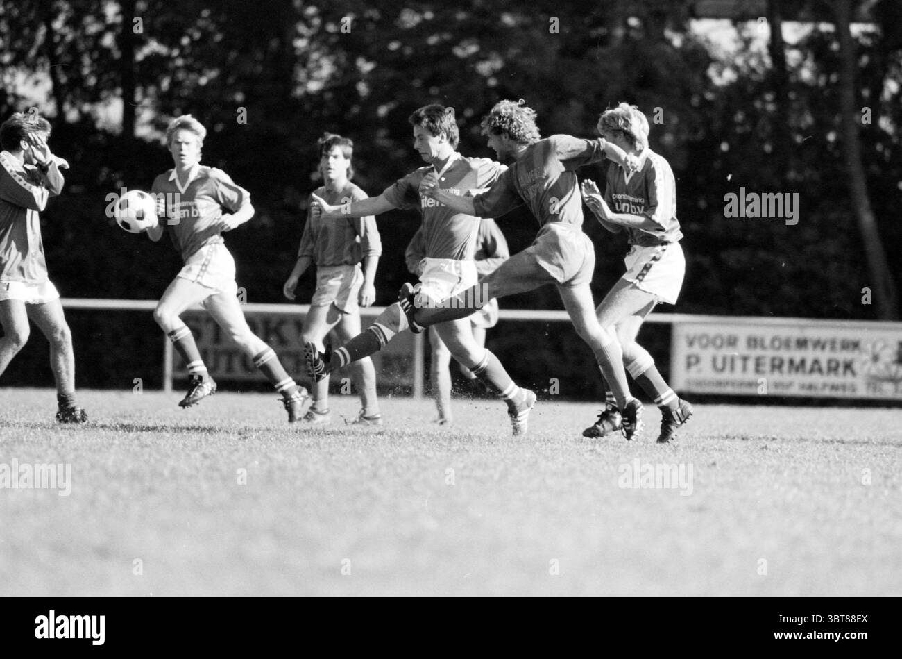 Halfweg - Zandvoort 75 Football, Whizgle News, Dutch Desk, Paesi Bassi, 1950 - 2000 il 05-10-1986. Questi argomenti vengono visualizzati nell'immagine. La scena raffigura una partita di calcio dinamica che si svolge su un campo erboso, in cui diversi giocatori sono impegnati in un intenso momento di gioco. Gli individui sono vestiti principalmente con maglie rosse brillanti, un sorprendente contrasto con il verde vivido dell'erba. I loro shorts sono una tonalità più leggera, che suggerisce un'uniforme coordinata della squadra. Il giocatore in primo piano viene catturato a metà azione, eseguendo abilmente un calcio mentre si concentra sulla palla. La sua posizione indica atletica Foto Stock