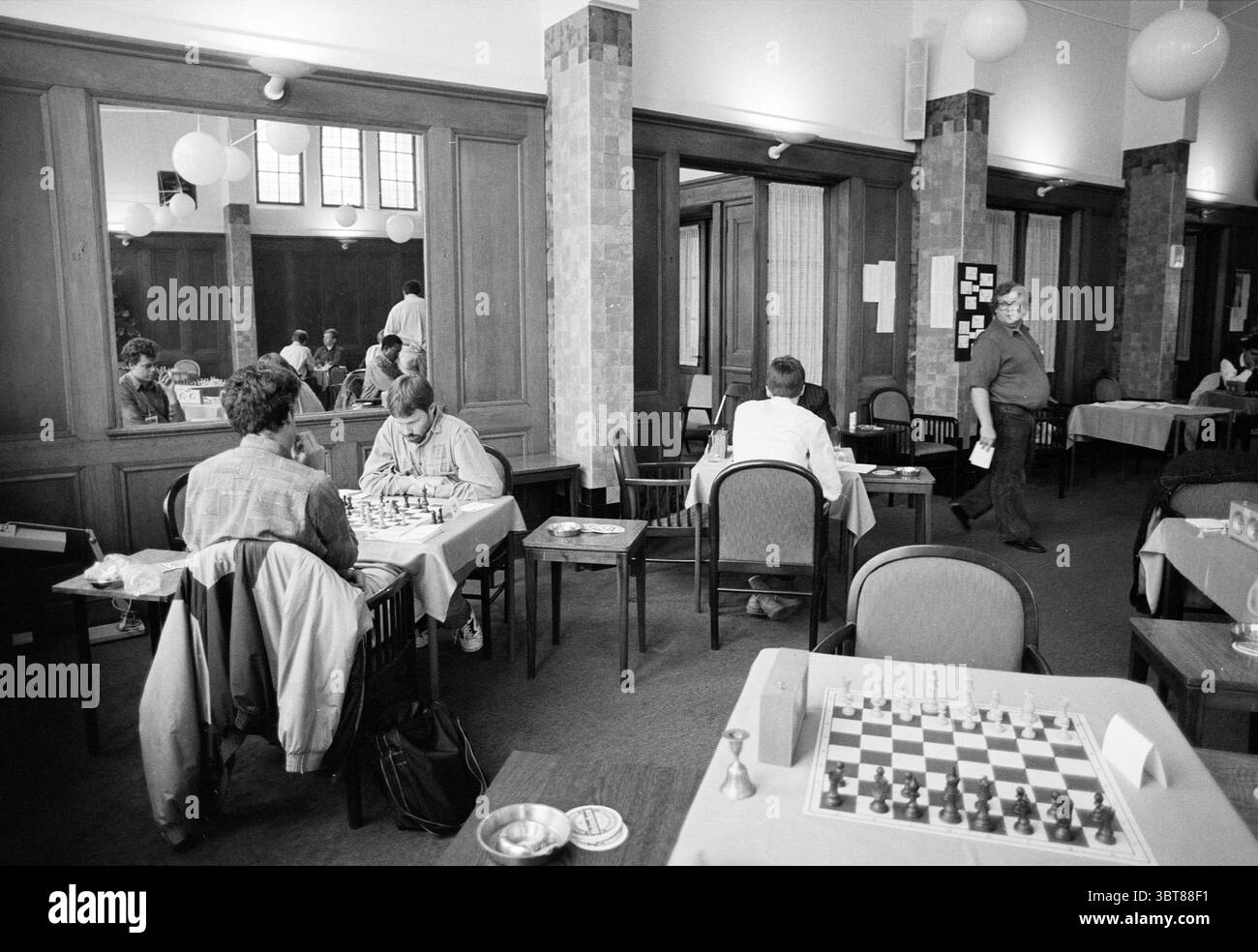AKN Chess Tournament Zijlweg 1 Haarlem Zijlweg, Whizgle News, Dutch Desk, Paesi Bassi, 1950 - 2000 il 18-06-1993. Questi argomenti vengono visualizzati nell'immagine. La scena è ambientata in una camera spaziosa e ben illuminata caratterizzata da un'atmosfera calda e invitante. I pannelli in legno fiancheggiano le pareti, contribuendo a creare un fascino del vecchio mondo, mentre le grandi finestre consentono alla luce naturale di inondare, diffondendo ombre morbide sul pavimento. In primo piano, due tavoli sono occupati da individui impegnati in una partita a scacchi. Un giocatore, con capelli ricci e un'espressione focalizzata, sta studiando la tavola con attenzione. Il suo avversario, un po' Foto Stock