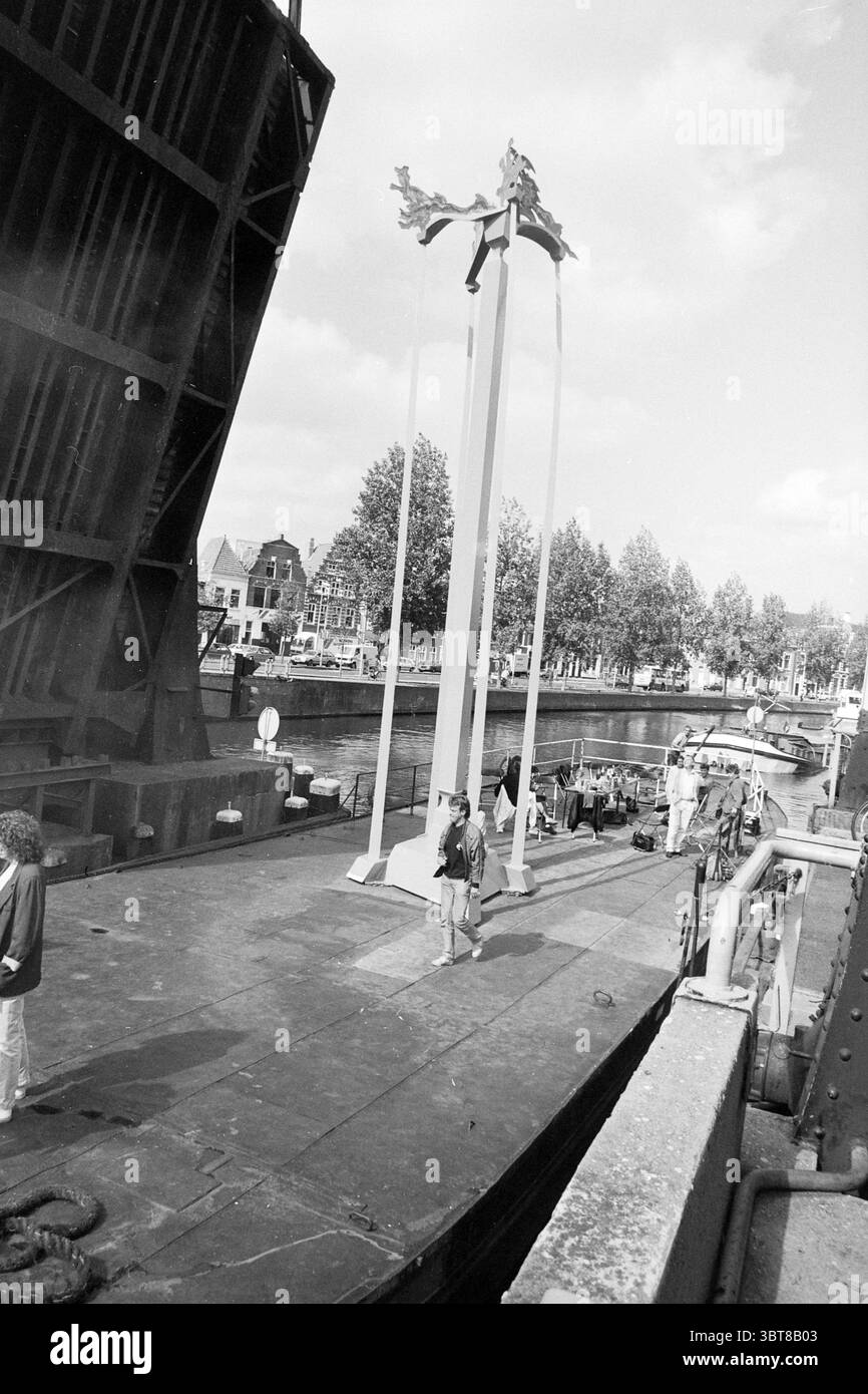 Trasporto di "oggetti d'arte" via nave attraverso la Spaarne, tra cui Drostefabriek, Whizgle News, Dutch Desk, Paesi Bassi, 1950 - 2000 nel 1991. L'immagine contiene questi argomenti. La scena cattura un momento in un vivace lungomare. In primo piano è visibile un'ampia area aperta di un molo o di un ponte di una nave, che rivela una superficie strutturata segnata dall'usura del tempo. Ci sono poche persone sparse in giro, impegnate in varie attività. Un individuo si erge centralmente, sembra contemplativo, vestito con abbigliamento casual, mentre un'altra persona viene vista camminare nelle vicinanze, aggiungendo un elemento di mo Foto Stock