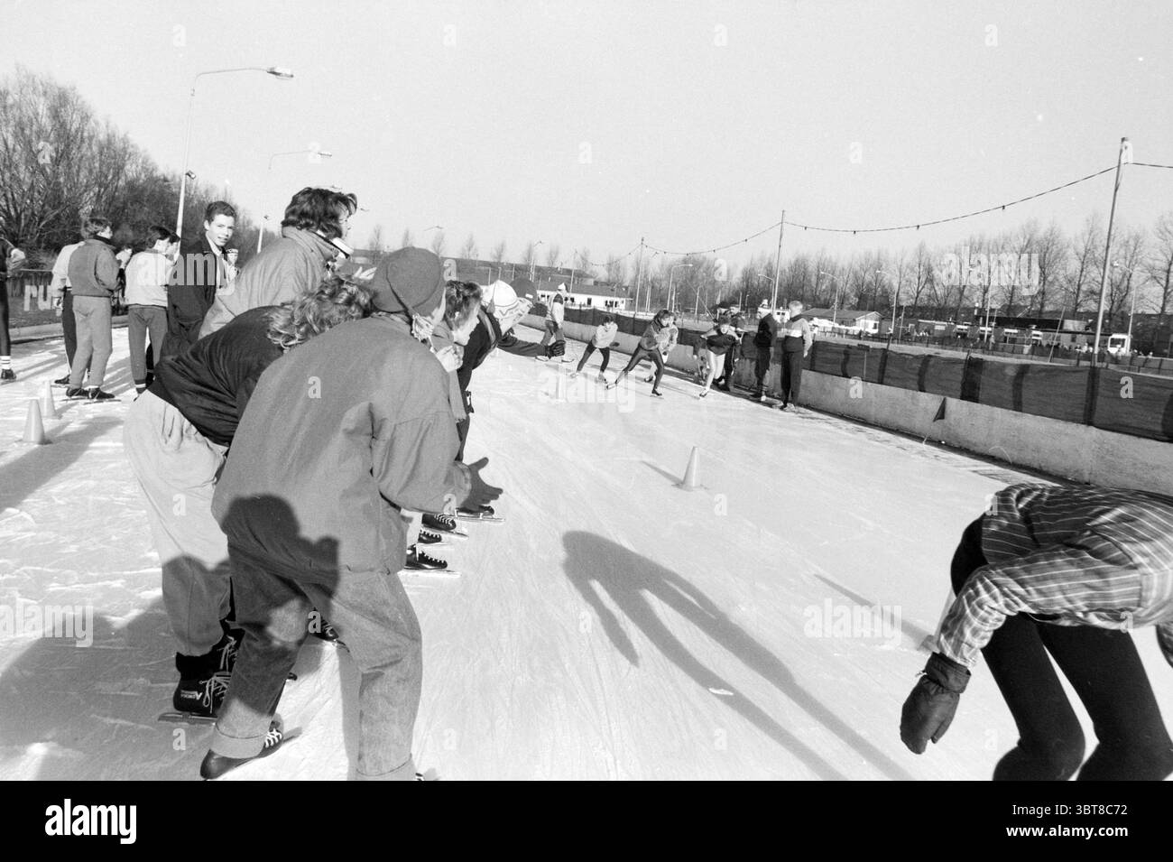 Gare di pattinaggio da 22 scuole pattinaggio, Whizgle News, Dutch Desk, Paesi Bassi, 1950 - 2000 il 30-01-1987. Questi argomenti sono mostrati nell'immagine. La scena raffigura una pista di pattinaggio su ghiaccio all'aperto, piena di attività. I gruppi di pattinatori scivolano con grazia sulla superficie riflettente, i loro movimenti variavano: Alcuni sono impegnati in corse animate mentre altri pattinano a un ritmo più rilassato. La tavolozza dei colori è dominata da sfumature monocromatiche di nero, bianco e grigio, che catturano un senso di nostalgia e chiarezza nell'aria fredda. Il ghiaccio scintilla sotto la luce del giorno, riflettendo il raggio del sole Foto Stock