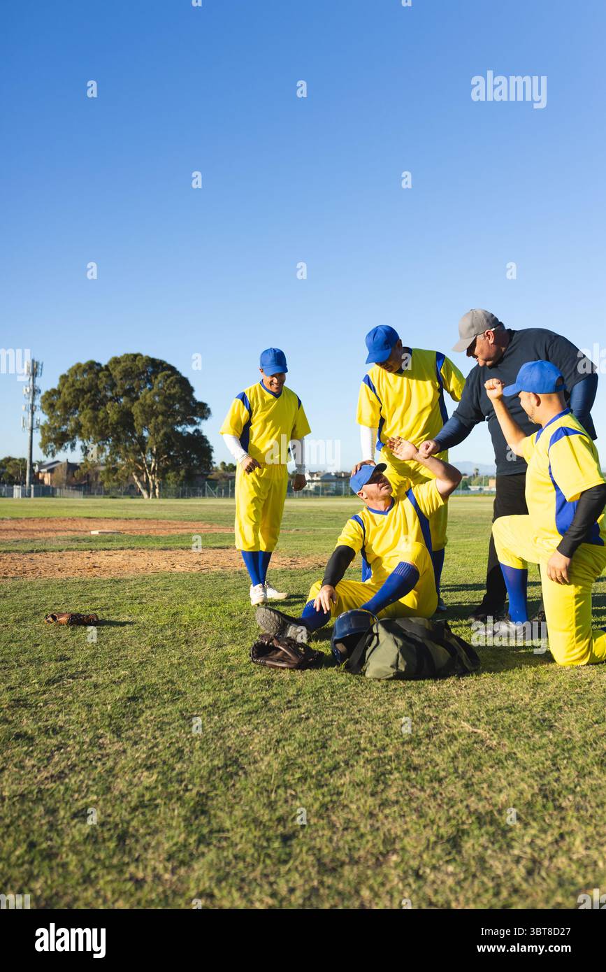 Compagni di squadra e allenatore di baseball maschili che si congratulano con il giocatore seduto sul campo con un guanto e una borsa sportiva Foto Stock