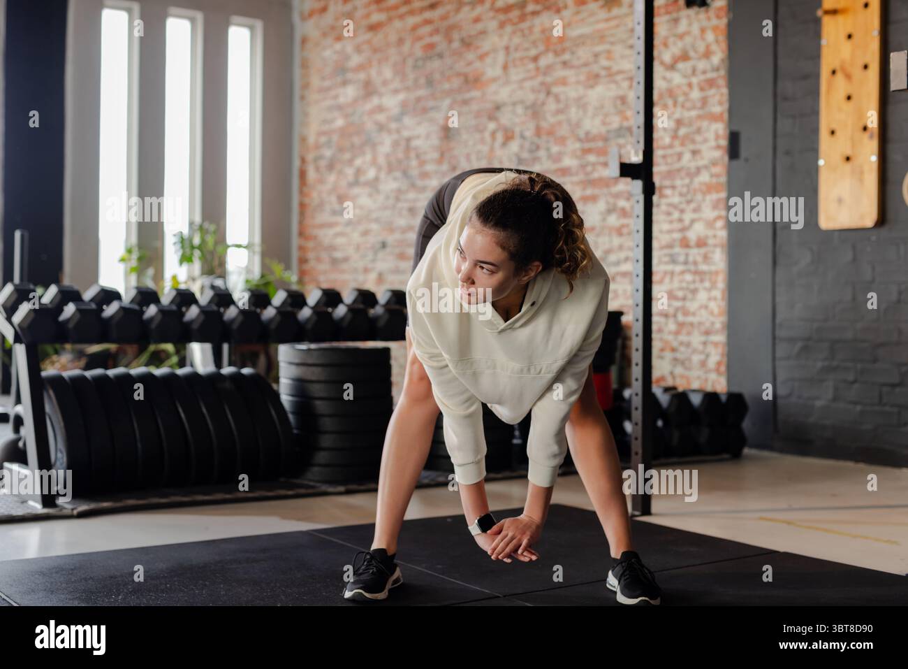 Donna che si piega in avanti su un tappetino in gomma da palestra con felpa con cappuccio e pantaloncini neri su un portamonete Foto Stock