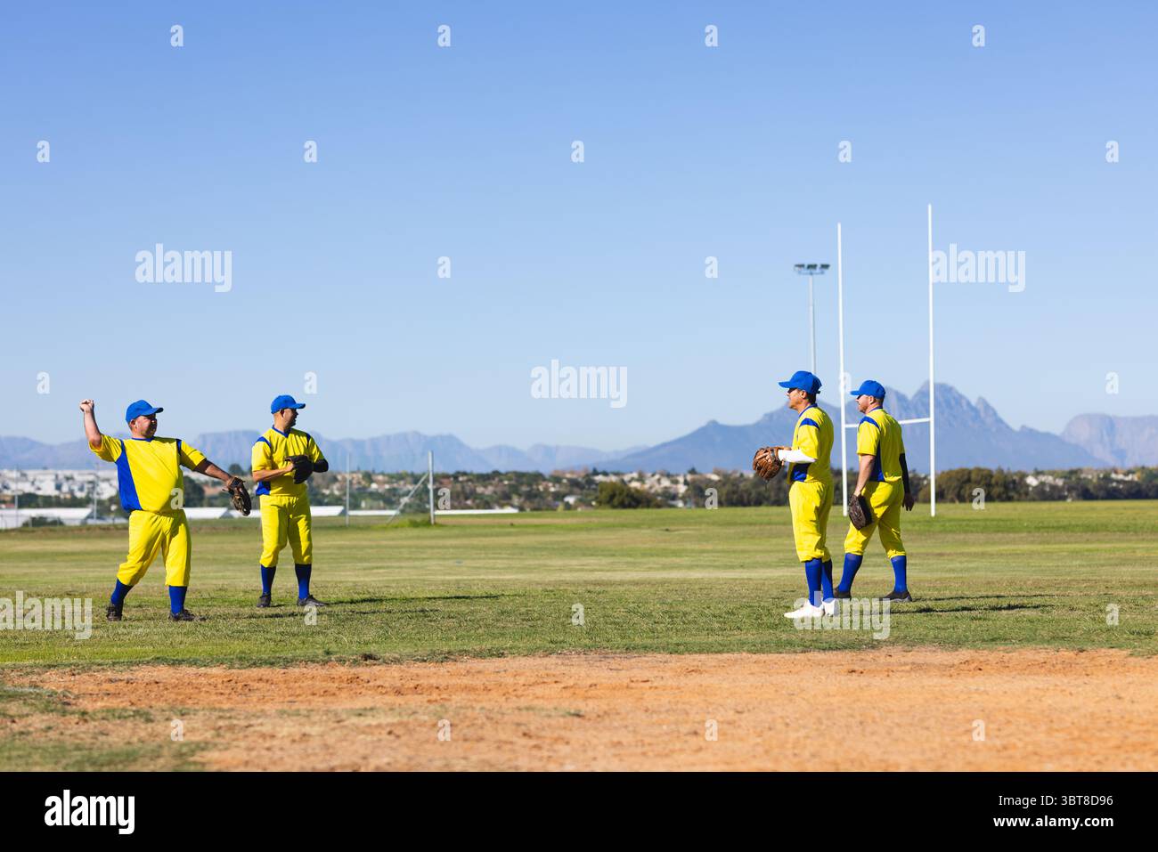 Diversi compagni di squadra maschili in uniforme giallo-blu in piedi sul campo tenendo i guanti sotto le pali da rugby Foto Stock