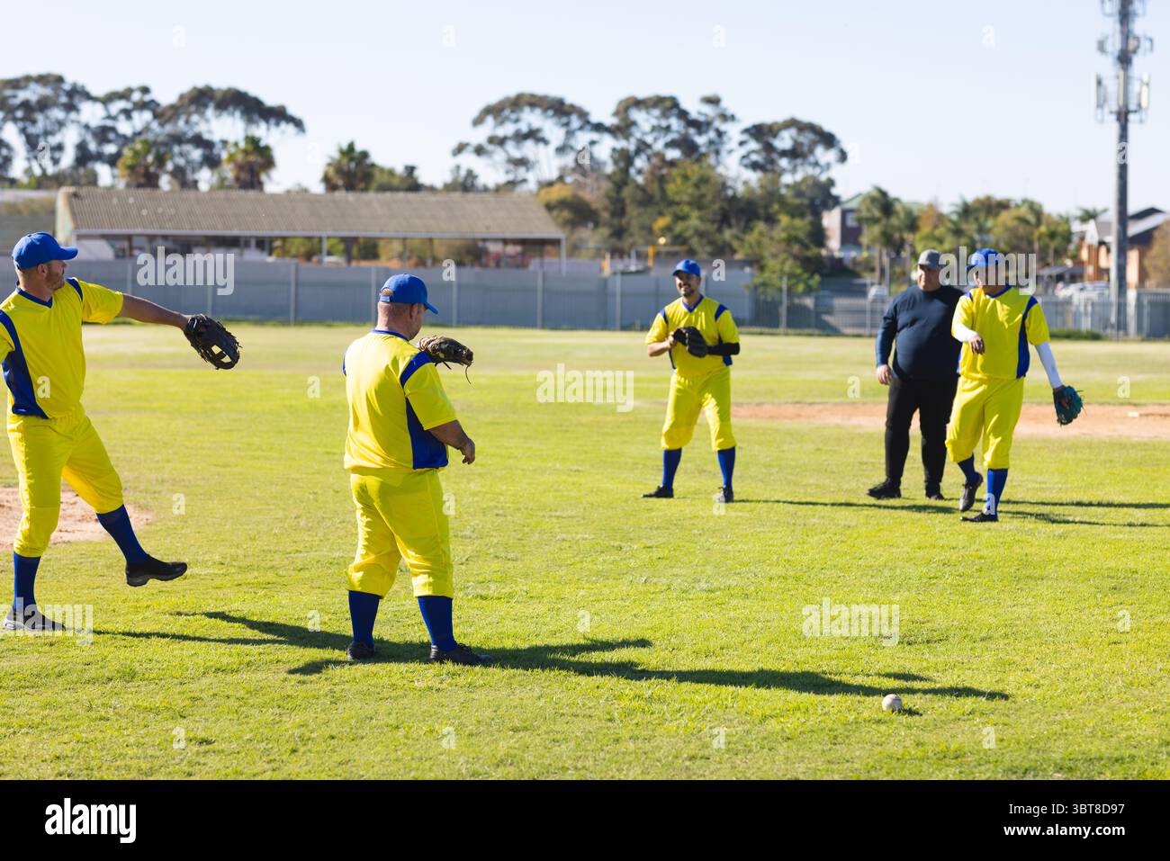 Squadra di baseball maschile e allenatore in piedi sul campo suburbano catturando il baseball con guanti e berretti Foto Stock