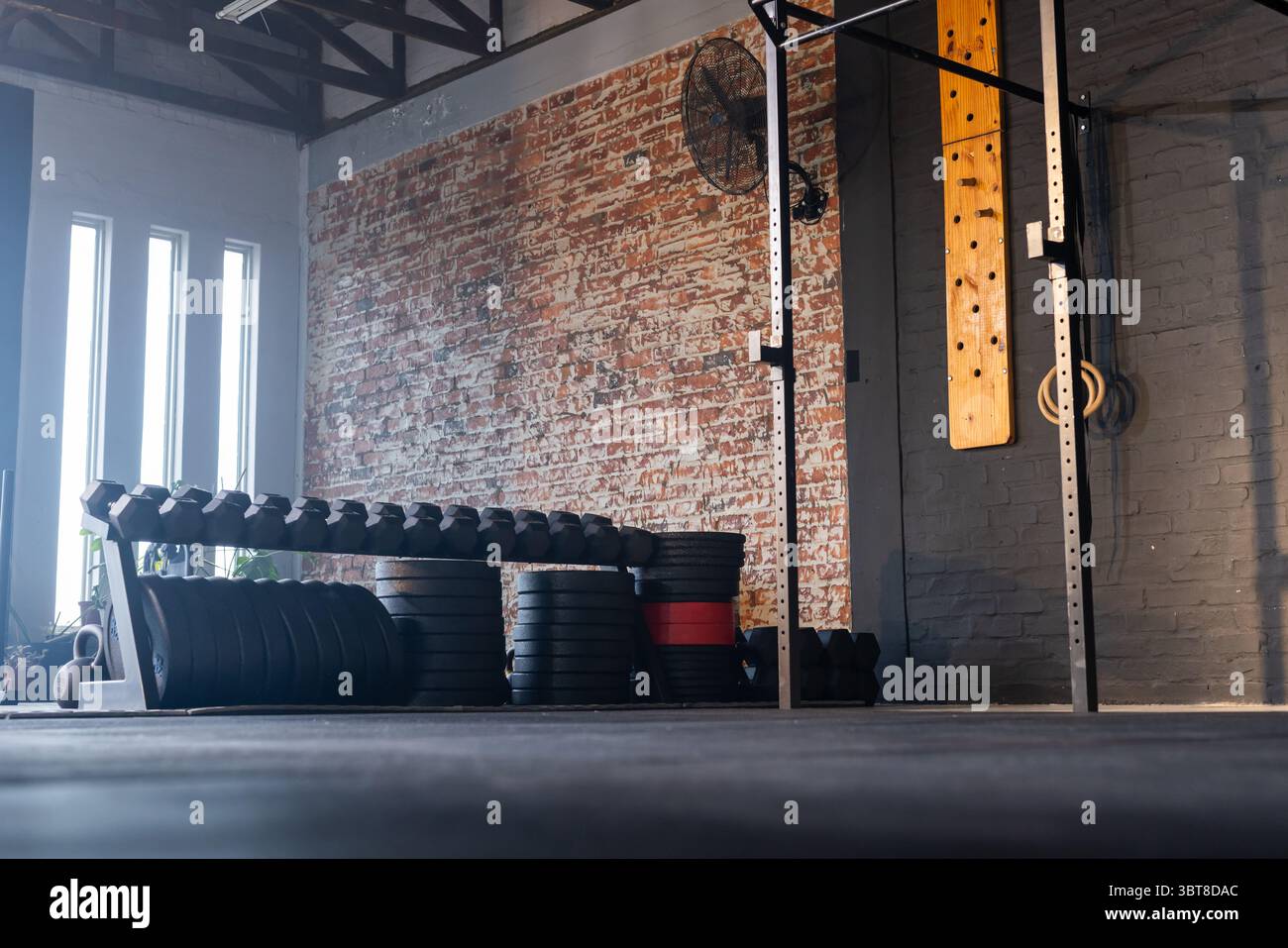 Rack per manubri con manubri e piastre per pesi impilate in una palestra funzionale con ventilatore industriale Foto Stock