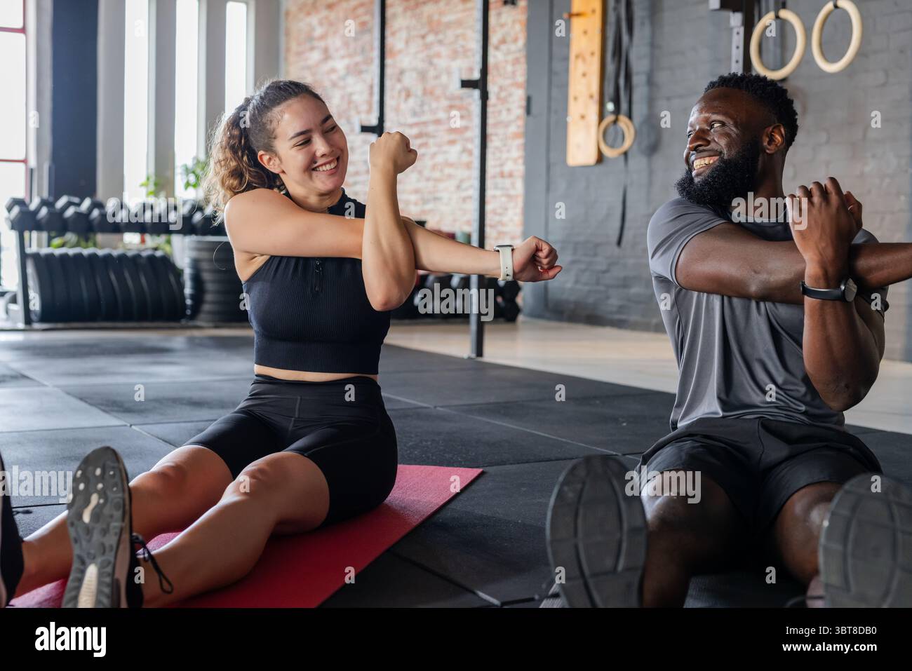 Diversi amici che eseguono il braccio trasversale sui tappetini in gomma in palestra con manubri Foto Stock