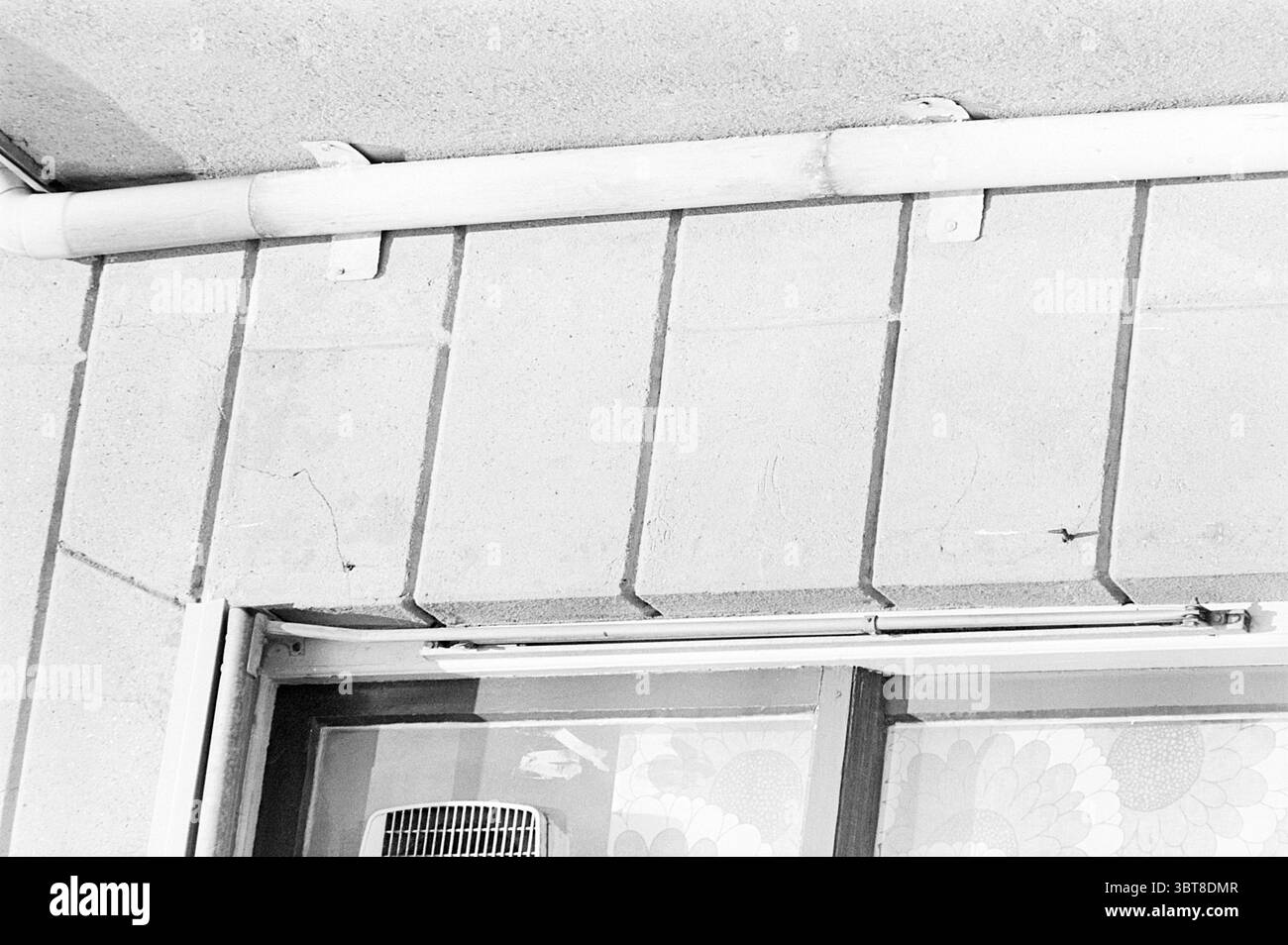 Edifici e crepe Nieuwe Gracht 49 - 51 Haarlem Huizen Haarlem Haarlem Nieuwe Gracht Paesi Bassi, Whizgle News, Dutch Desk, Paesi Bassi, 1950 - 2000 il 05-08-1977. L'immagine contiene questi argomenti. La scena presenta una parete testurizzata realizzata in blocchi di cemento, che mostra una serie di linee orizzontali e verticali che creano un motivo ritmico. I blocchi sono di colore chiaro, conferendo un tono neutro che contrasta con le ombre fredde sparse sulla superficie. Nell'angolo superiore sinistro, un tubo bianco corre lungo il bordo, la sua finitura liscia contrasta con la rugosità della parete. I giunti Foto Stock