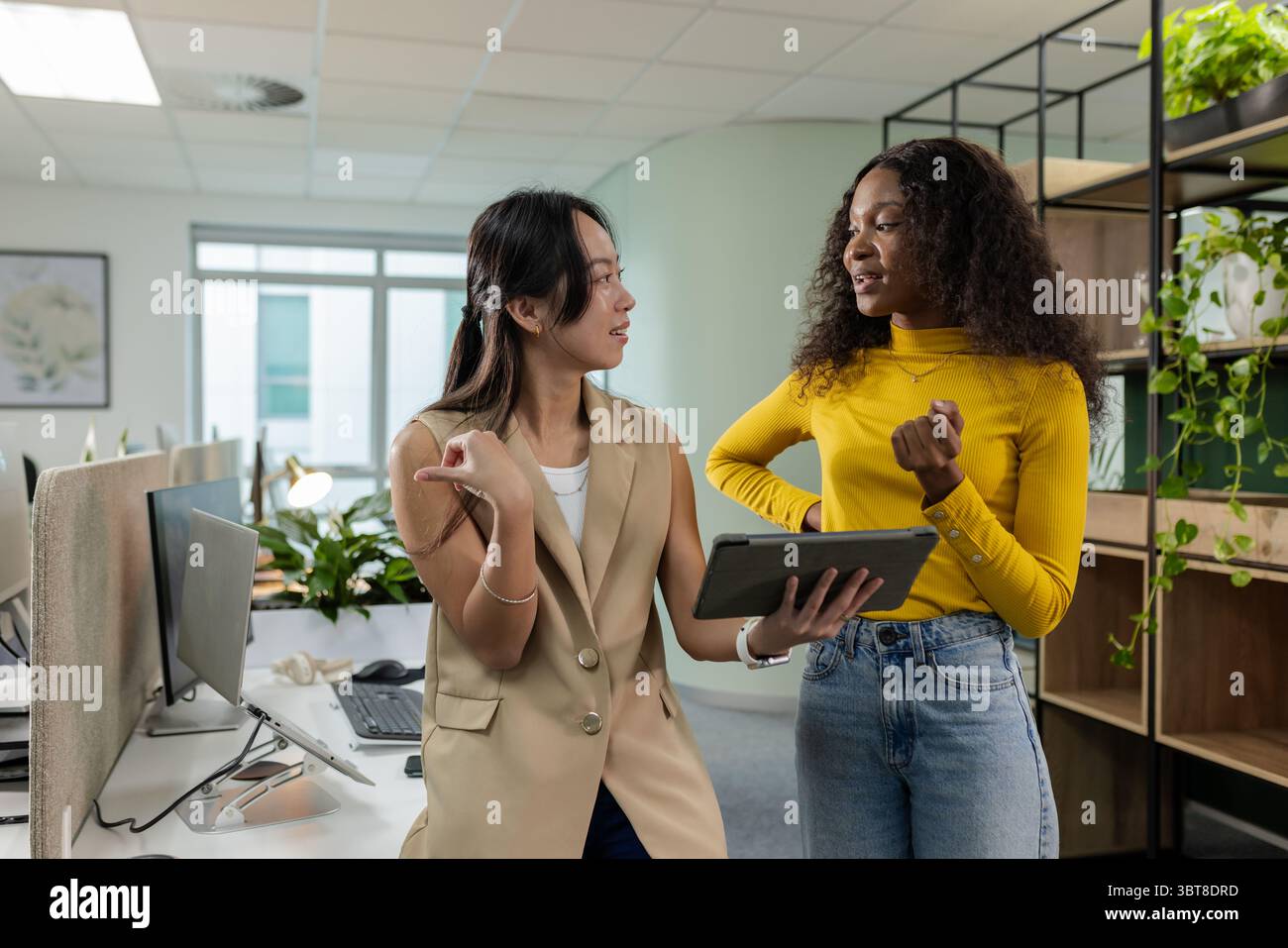 Diverse collaboratrici che discutono di strategie su tablet accanto alle scrivanie in un ufficio open space Foto Stock