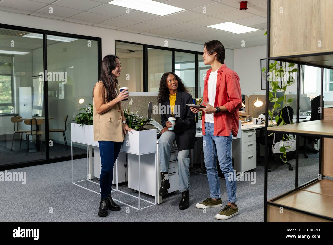 Diversi colleghi che chiacchierano in un moderno ufficio open-space con tazze, smartphone e pasticceria da portare sempre con sé Foto Stock