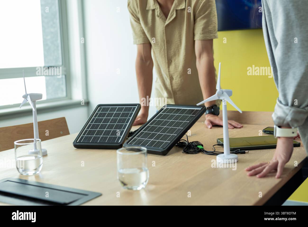 Colleghi asiatici che si appoggiano al tavolo in ufficio esaminando i pannelli solari pieghevoli e i modelli di turbine eoliche Foto Stock