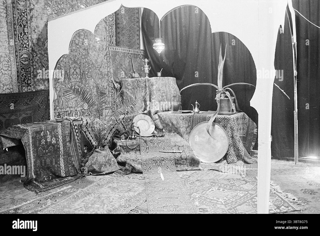 Scuola diurna turca Haarlem Schools, Whizgle News, Dutch Desk, Paesi Bassi, 1950 - 2000 il 30-03-1971. Questi argomenti vengono visualizzati nell'immagine. La scena presenta un ricco arazzo di texture e colori, creando un'atmosfera invitante ed esotica. Lo sfondo presenta drappi profondi e scuri che contrastano con i numerosi tappeti e tessuti con fantasie intricate disposti a strati sulla superficie. In primo piano, vari oggetti contribuiscono alla profondità culturale della scena. Un ampio vassoio in metallo dal design complesso si trova in modo prominente, riflettendo luce soffusa e circondato da una piccola sala cerimoniale Foto Stock